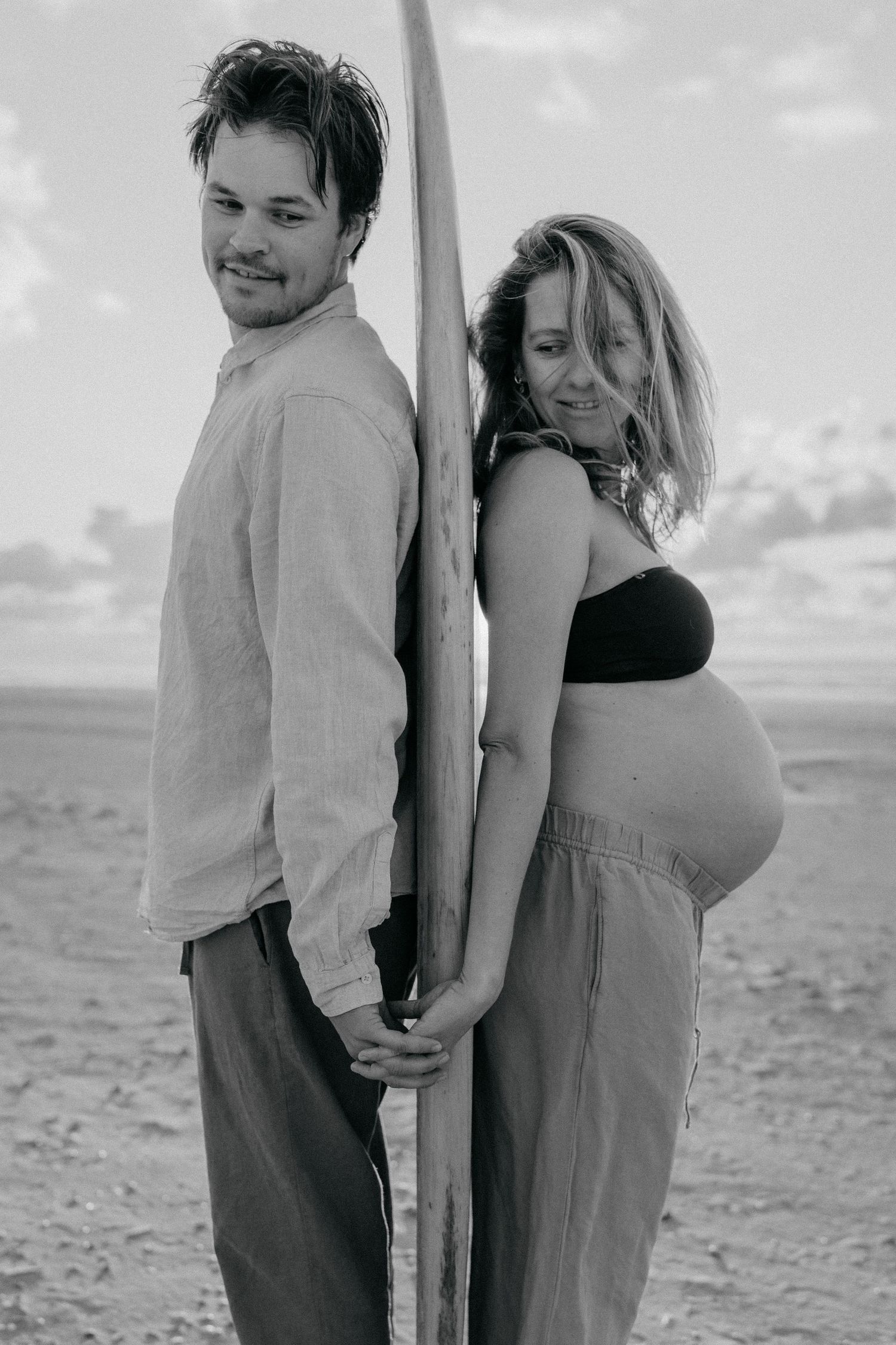 Adventurous surfer couple with surfboard during maternity shoot at the beach
