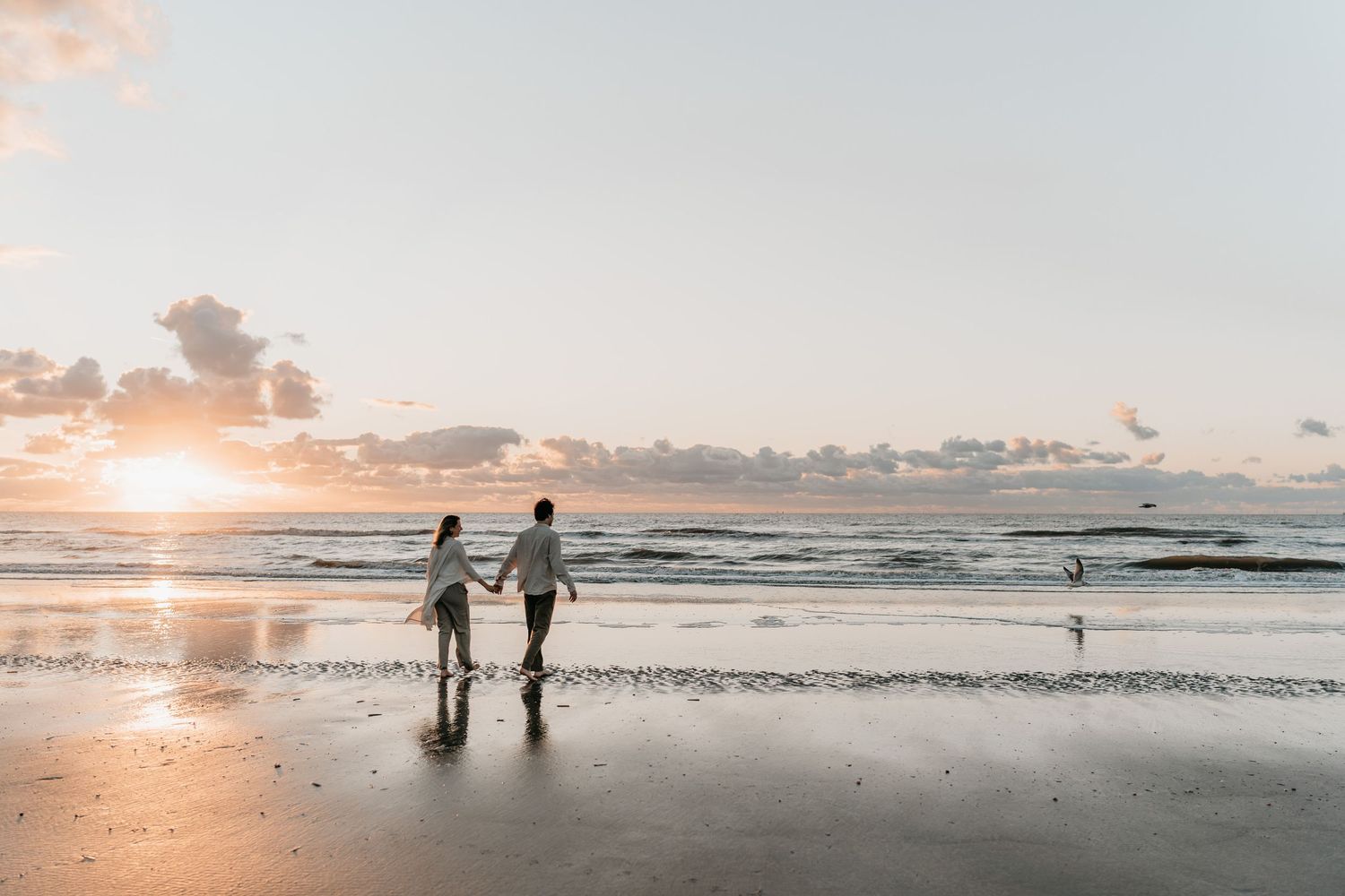 Koppel rent over het strand met vogels die opvliegen tijdens zwangerschapsfotoshoot