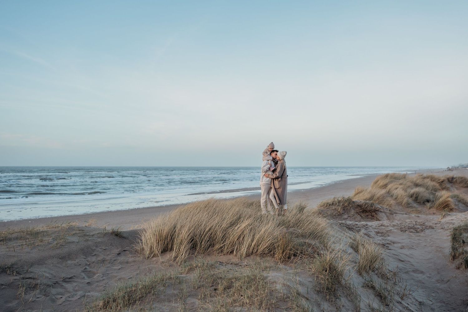 Een gezinsfoto aan het strand in de winter waarbij de ouders de kinderen knuffelen in de duinen met uitzicht op de zee