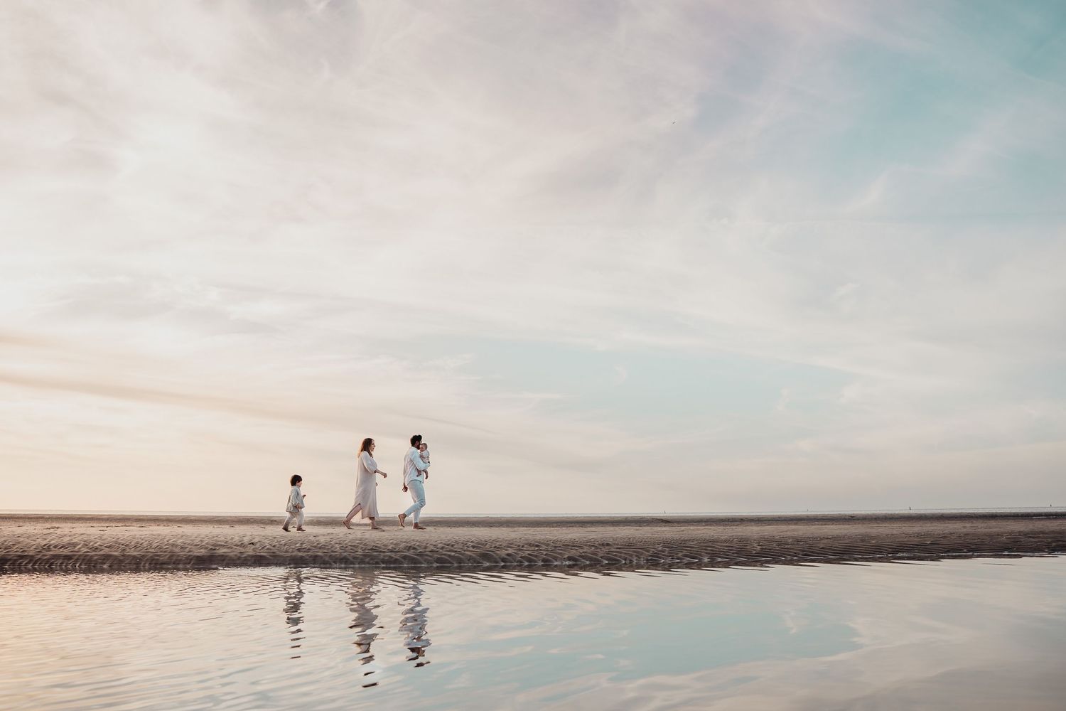 Een familieshoot aan het strand waarbij het gezin langs de kustlijn loopt en hun reflectie weerspiegelt in het water in Zeeland
