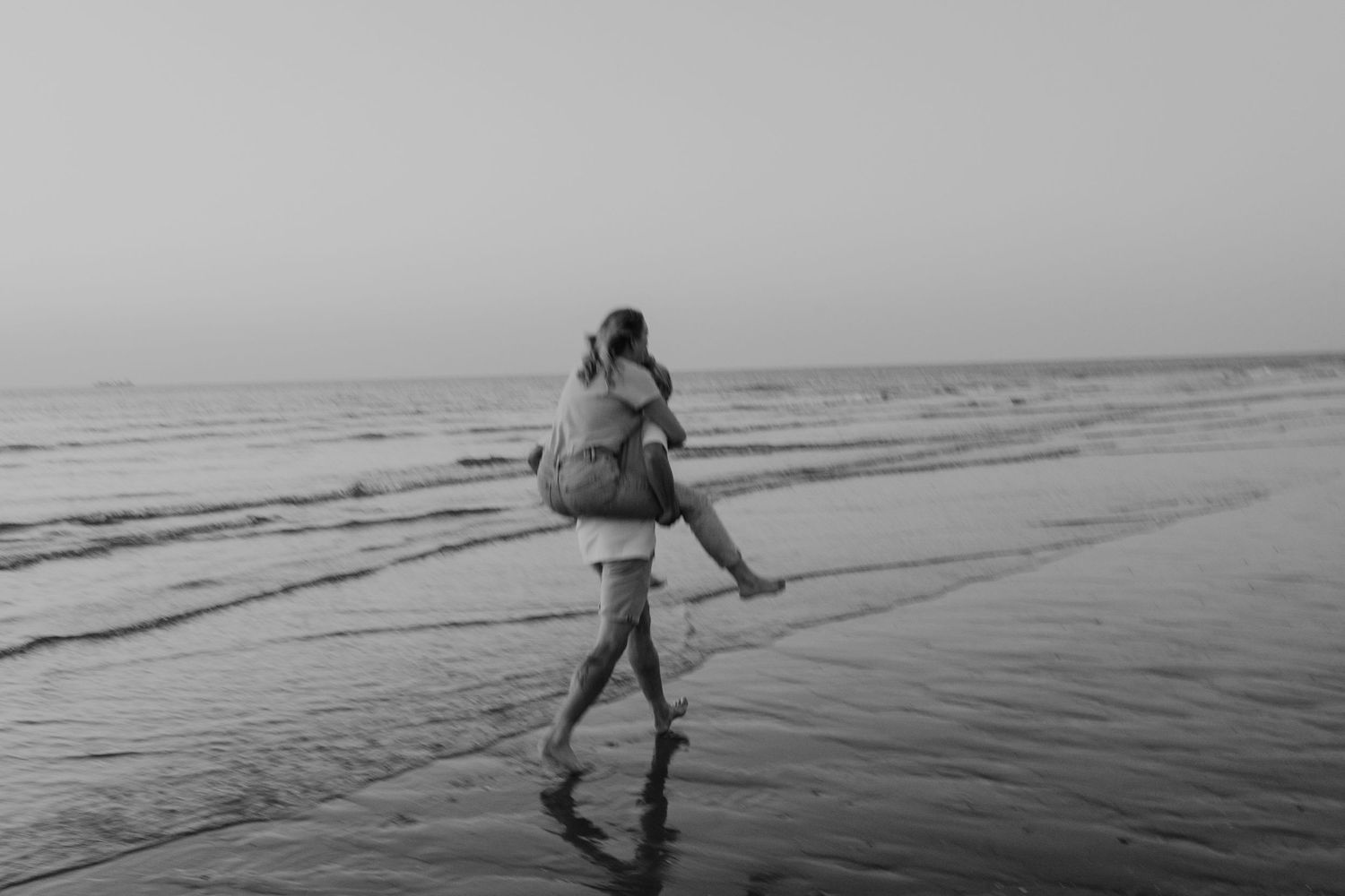 Zwart-wit foto van een verliefd koppel op het strand dat rent door de branding tijdens een fotoshoot