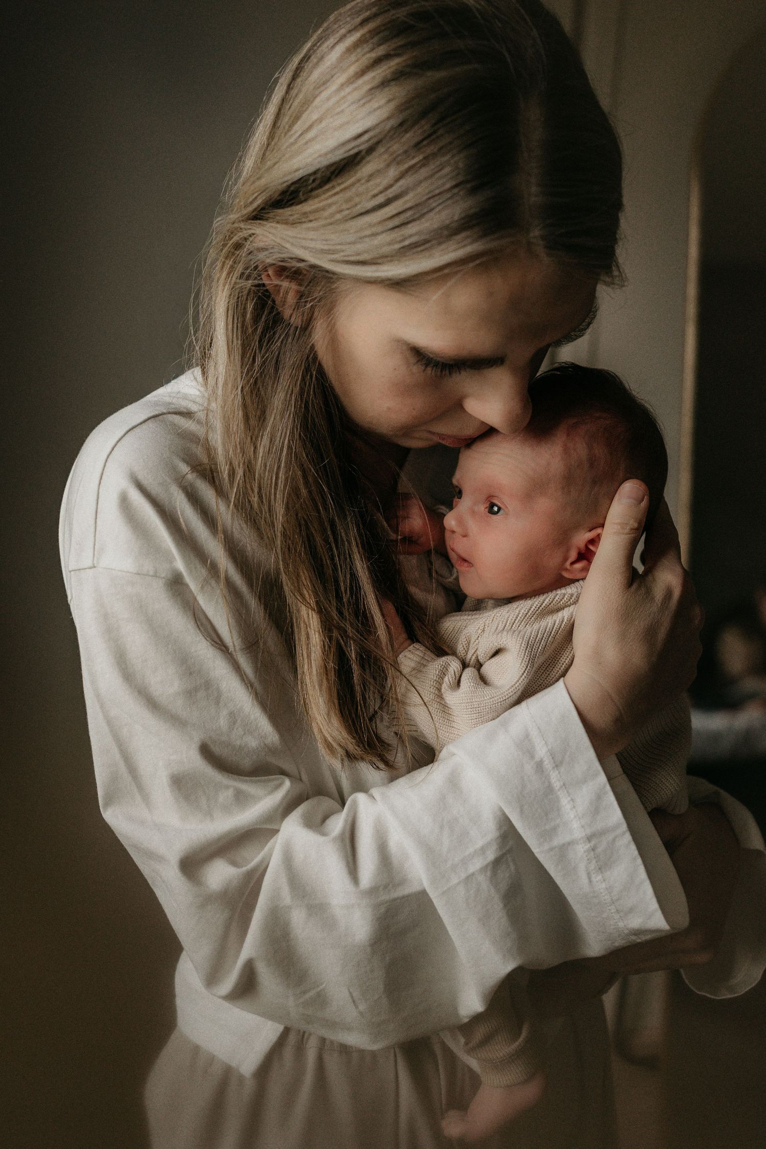 Moeder kijkt trots en beschermend naar pasgeboren dochter tijdens een newbornshoot