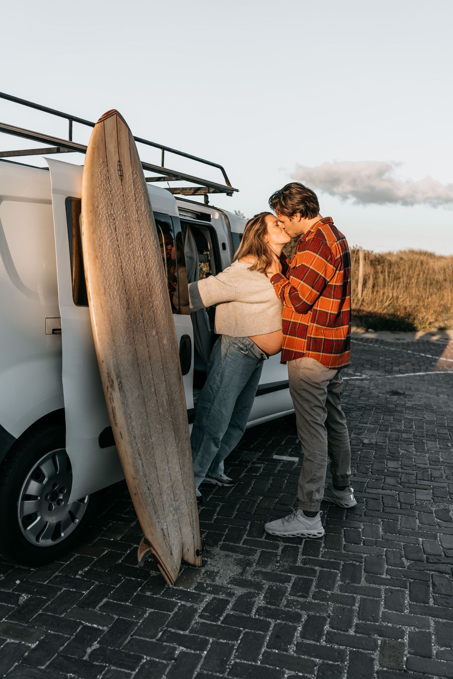 Adventurous van-life couple during maternity shoot at the beach with surfboards
