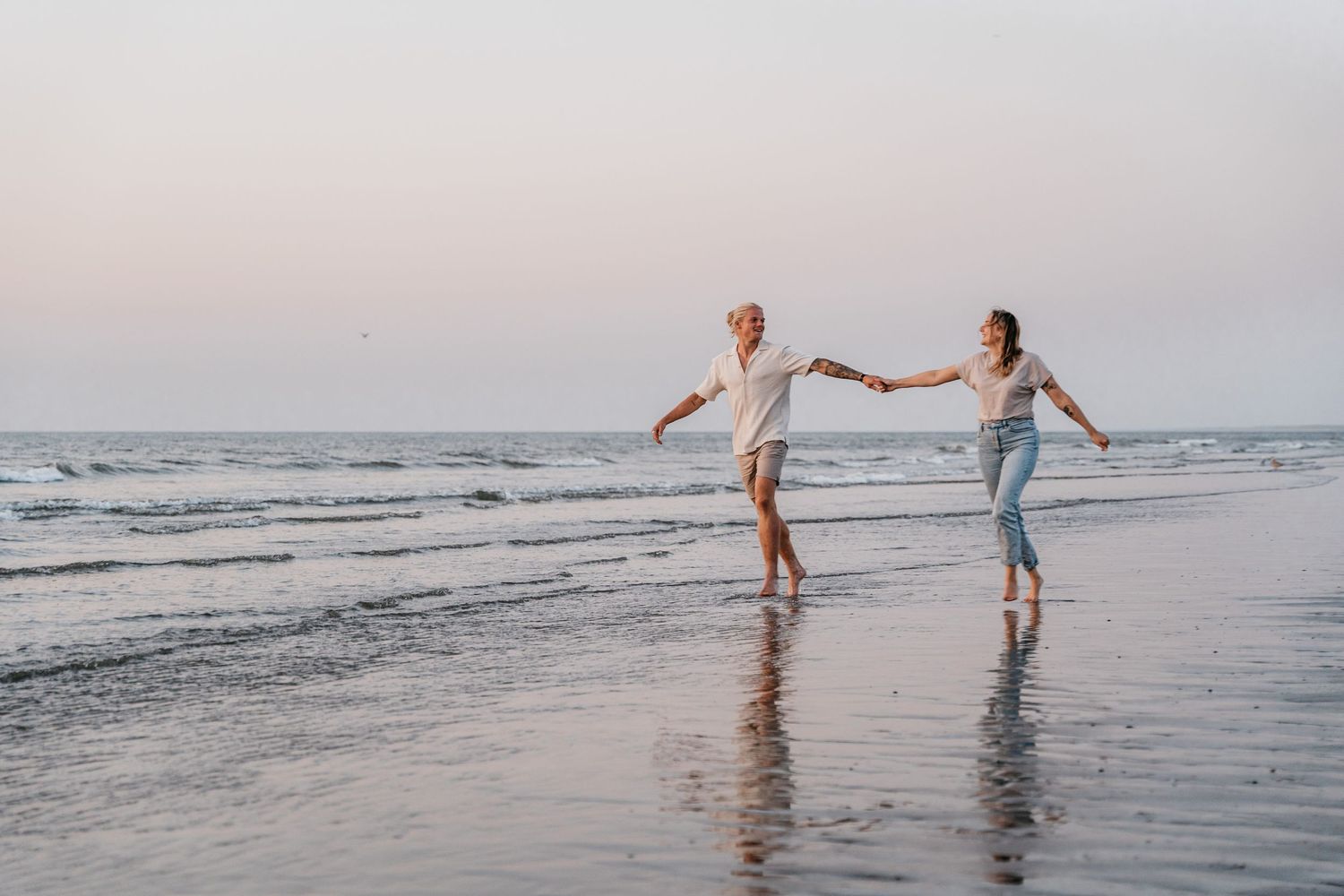 Fotoshoot van een verliefd koppel op het strand dat hand in hand door het water rent