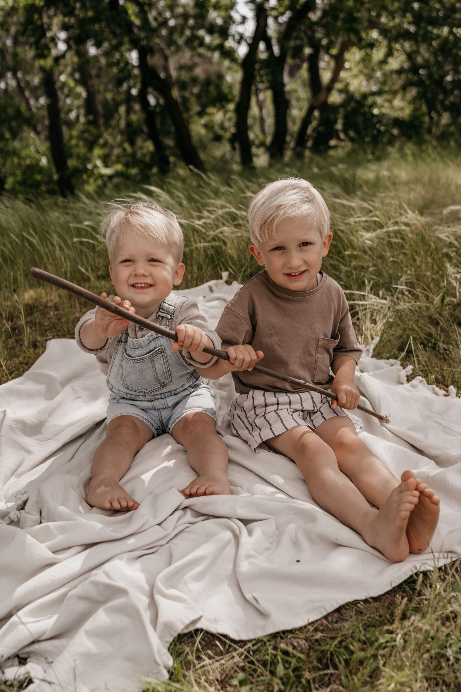 Twee broertjes spelen met een stok in het bos tijdens een fotoshoot op het Cadettenkamp bij Breda