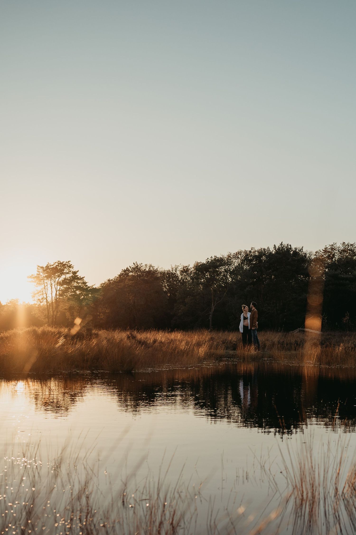 Een zwanger koppel in de natuur tijdens een zwangerschapsshoot met de ondergaande zon