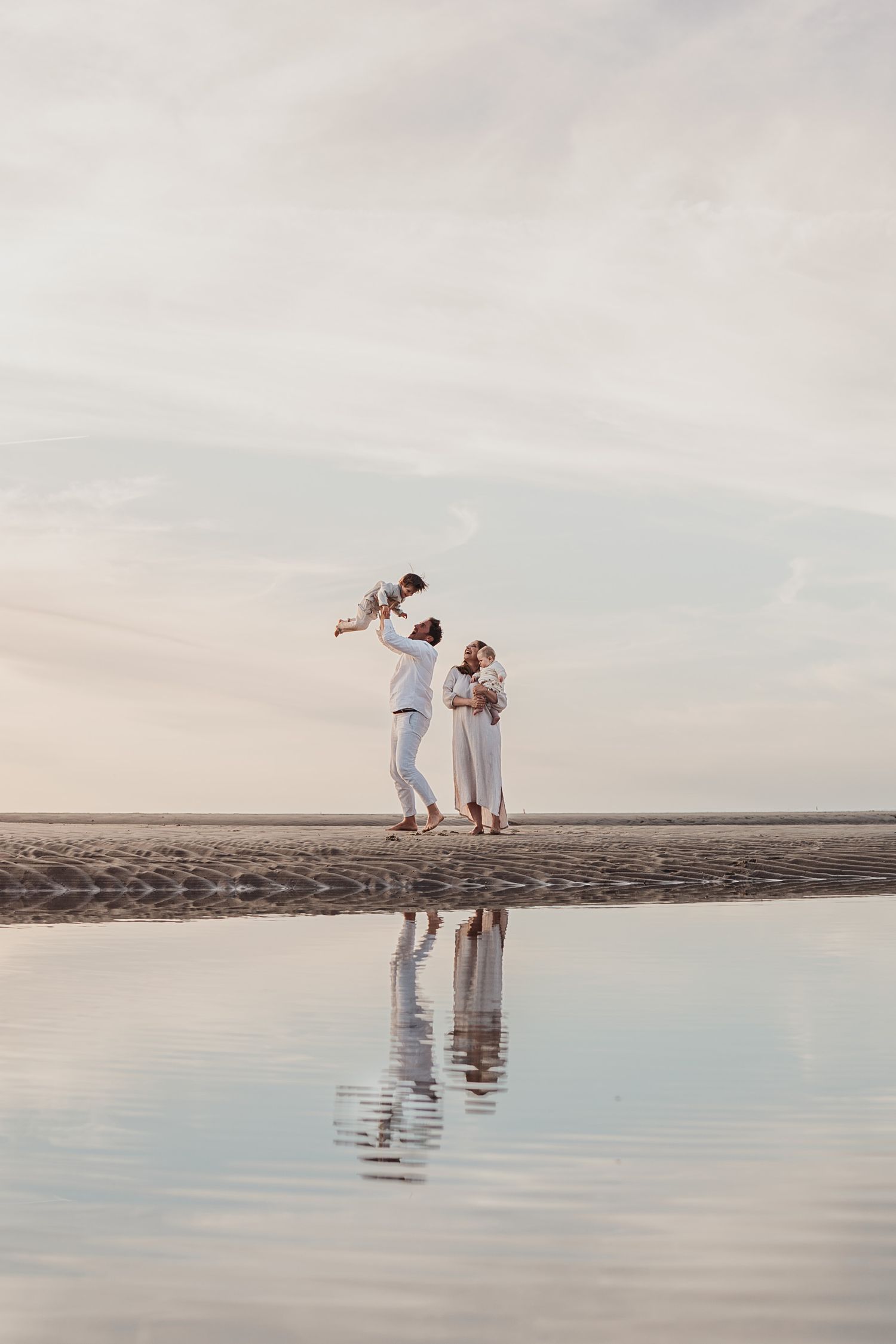Een spontane familiefoto waarbij een kindje in de lucht wordt getild tijdens een fotoshoot aan het strand in Ouddorp