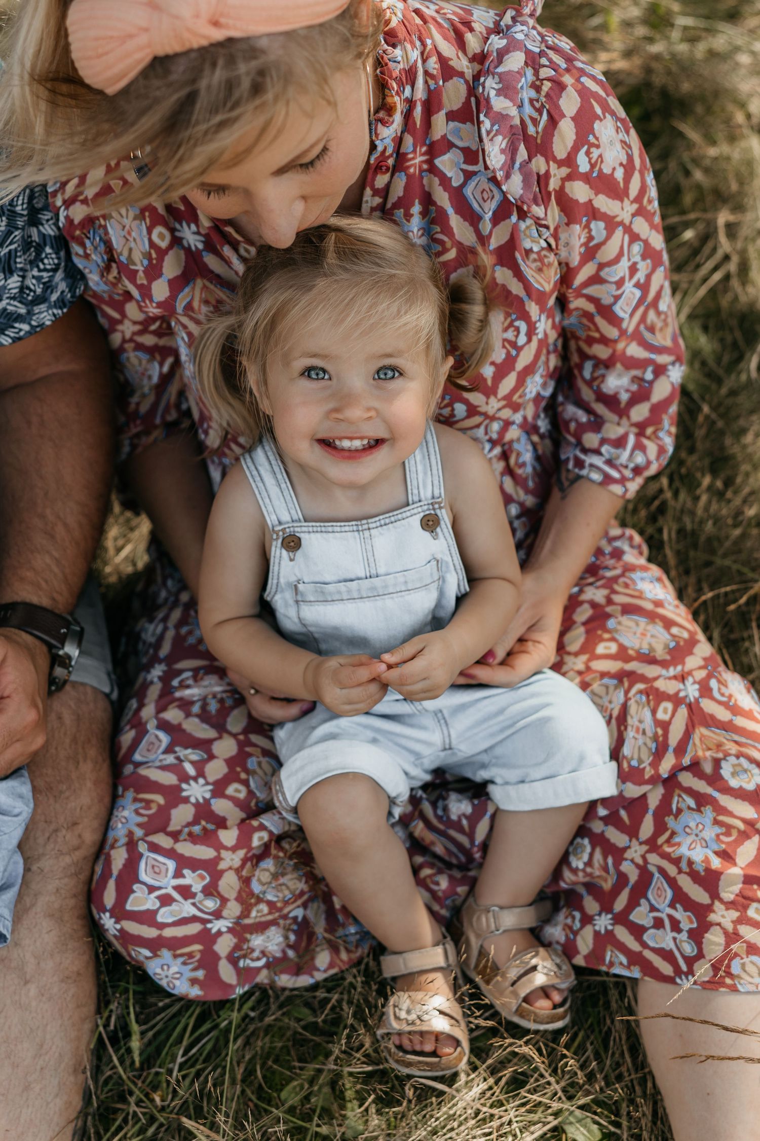 Lachende dochter kijkt in de camera terwijl ze bij haar moeder op schoot zit die liefdevol naar haar kijkt tijdens een familieshoot in Breda