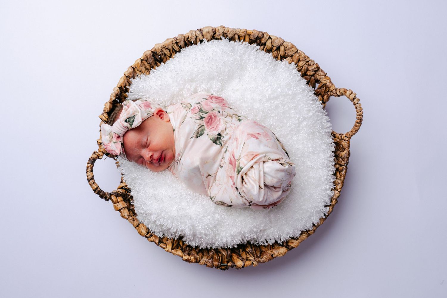 Six small white oval woven baskets arranged side by side containing soft white fabrics and textures.