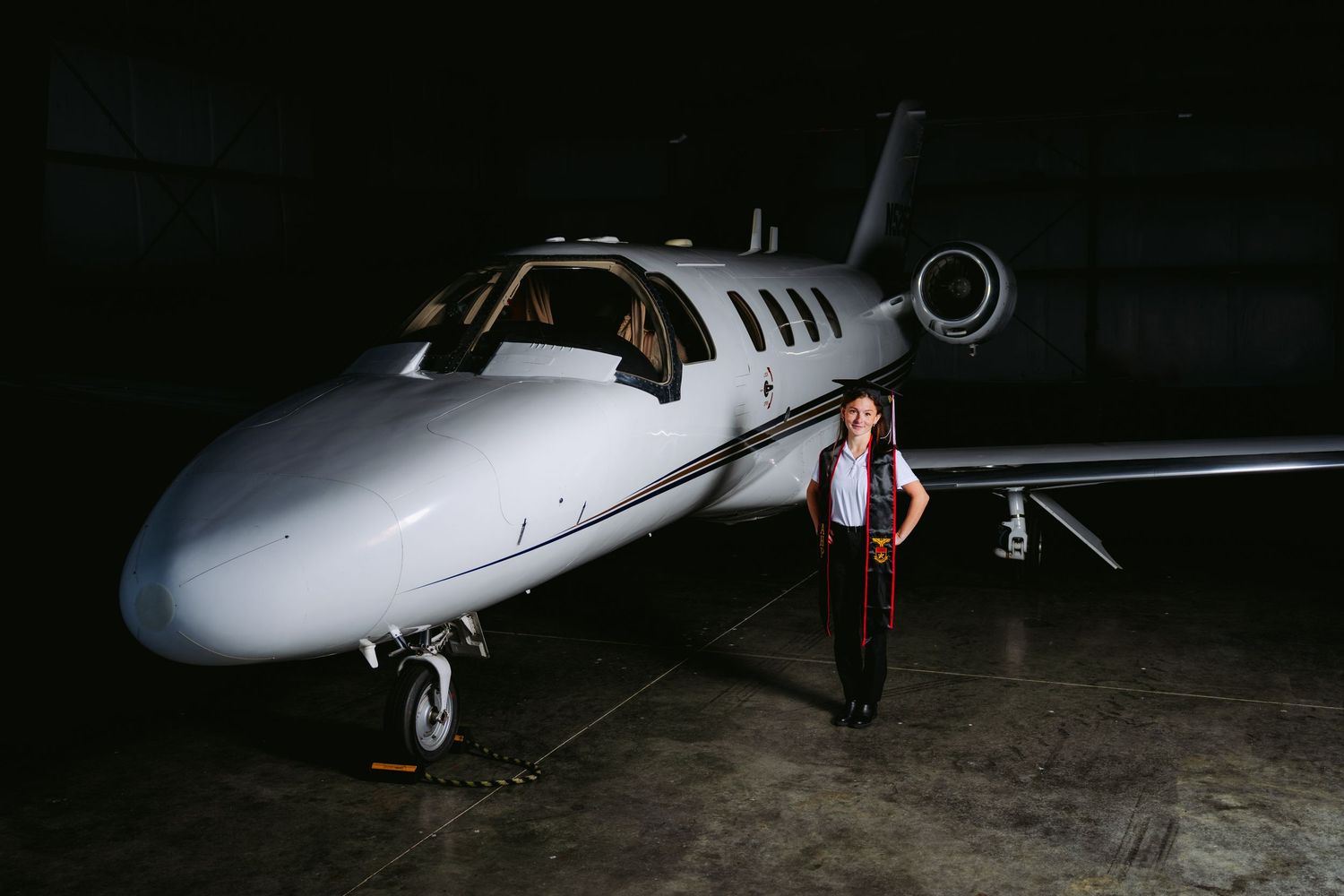 Private jet aircraft parked in dark hangar with figure standing beside it at night.