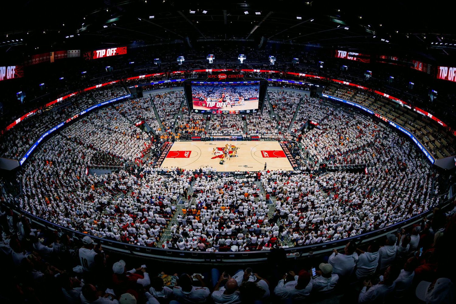 Aerial view of a packed basketball arena with red court during a game showing crowded white-out themed stands.