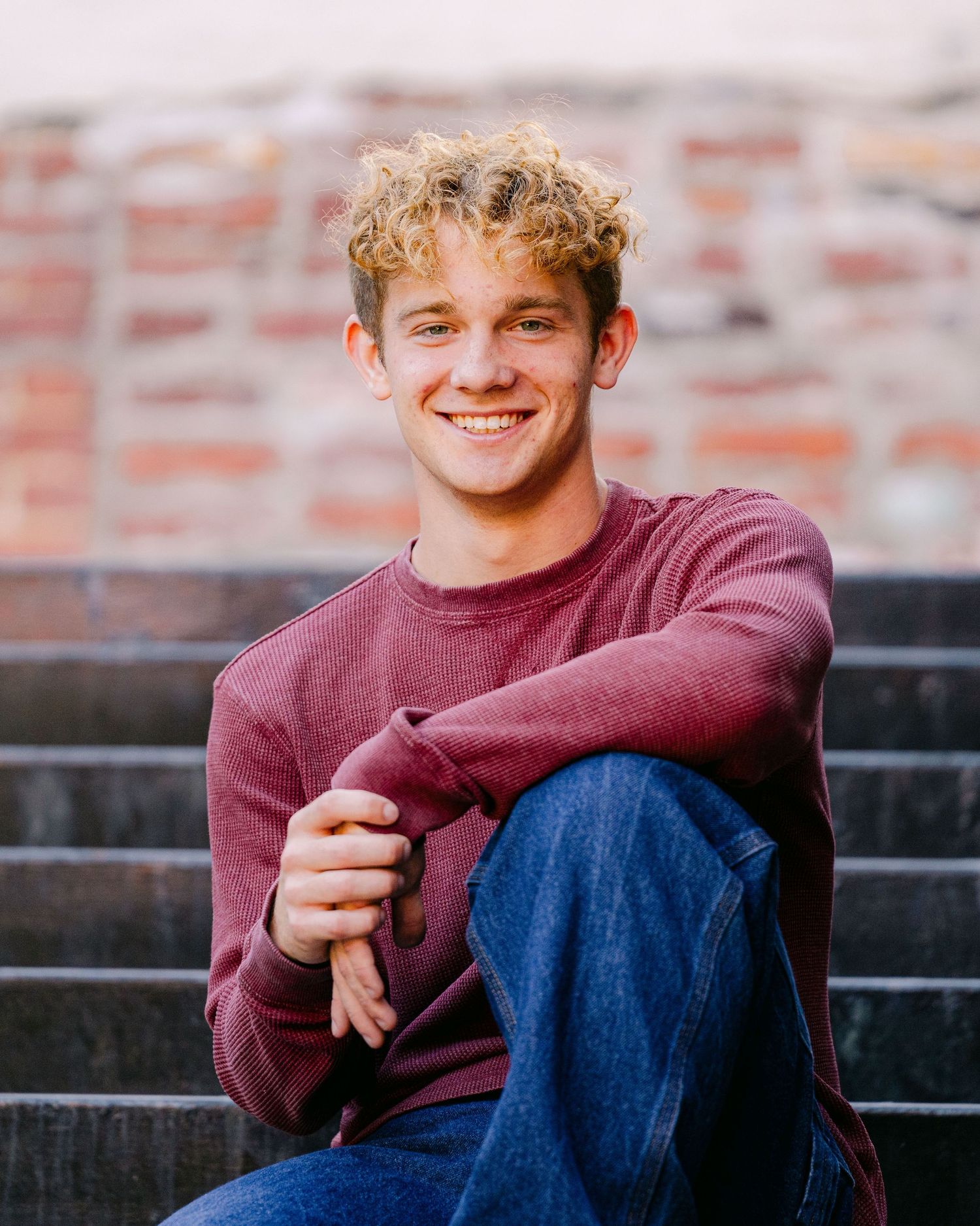 Casual portrait on brick steps wearing burgundy sweater and jeans.