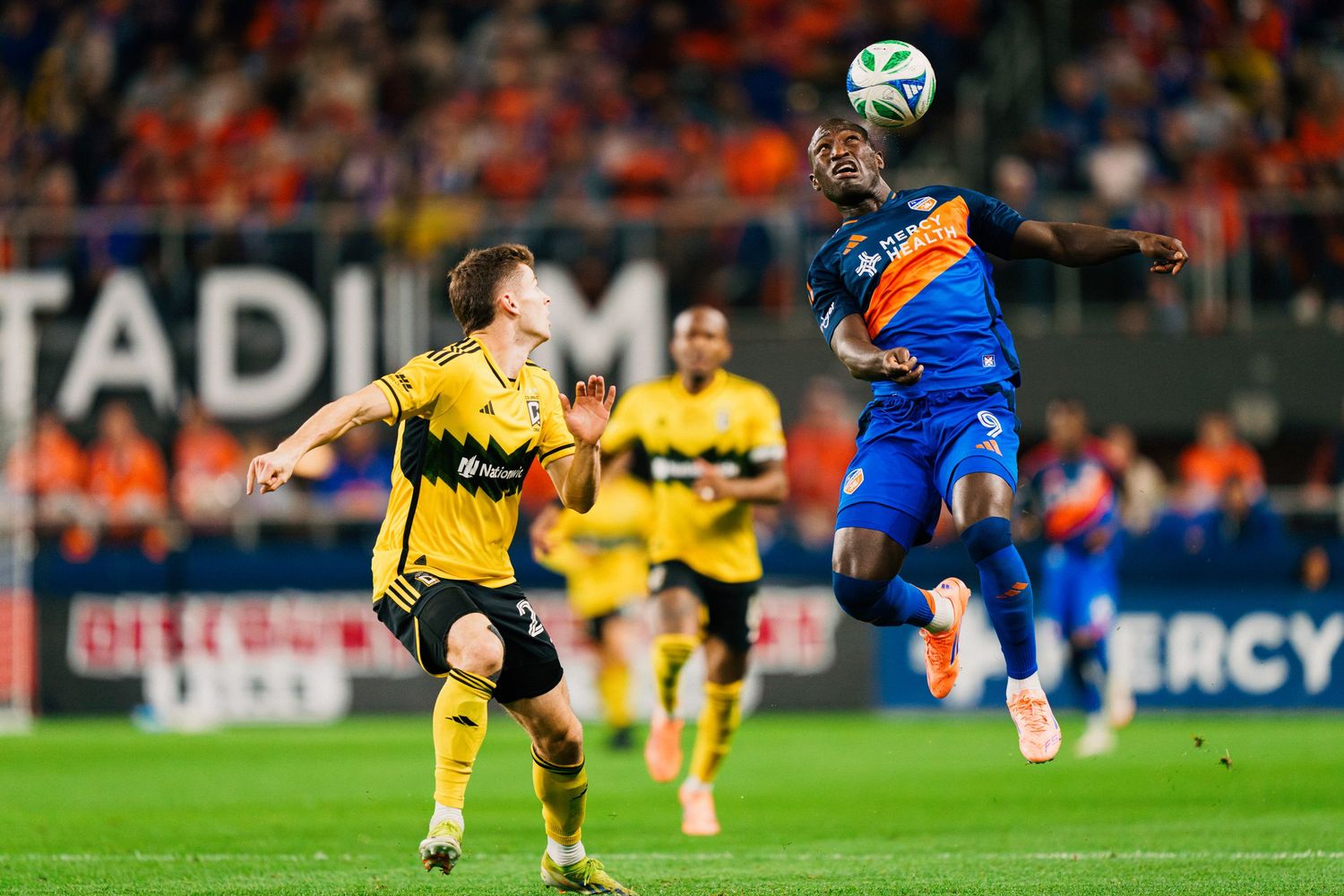 Two soccer players compete for control of the ball during an intense match at a stadium.