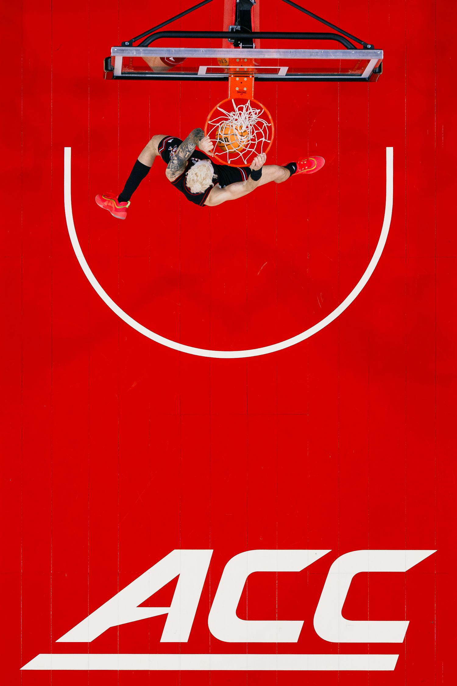 Basketball players jump to make a shot against a vibrant red background with white court markings.