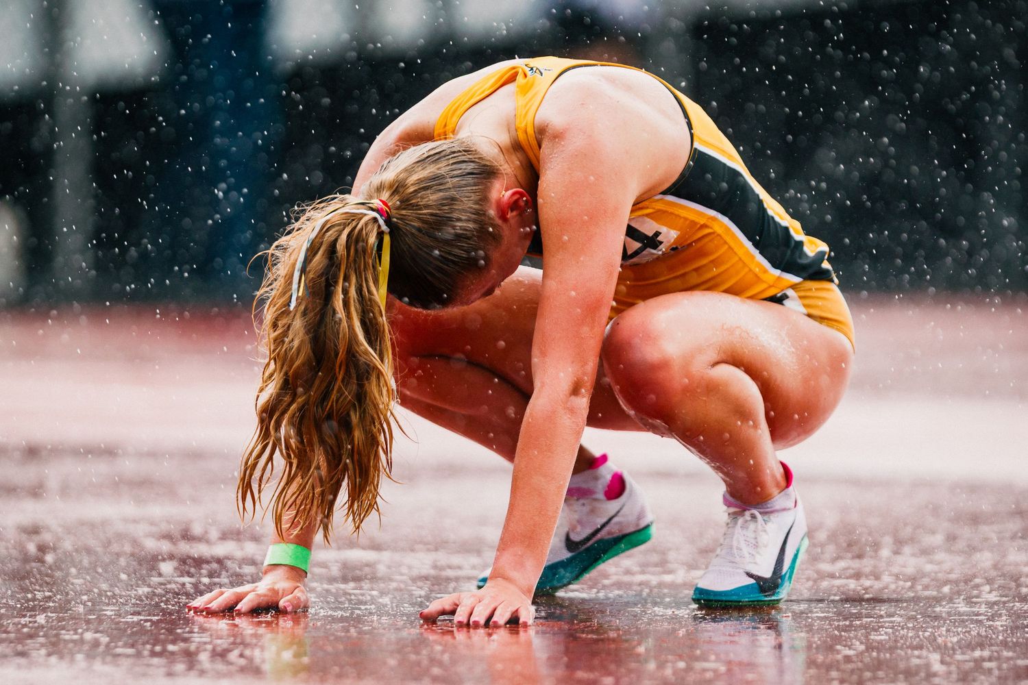 Athlete in orange uniform crouches on wet track during rainy competition.