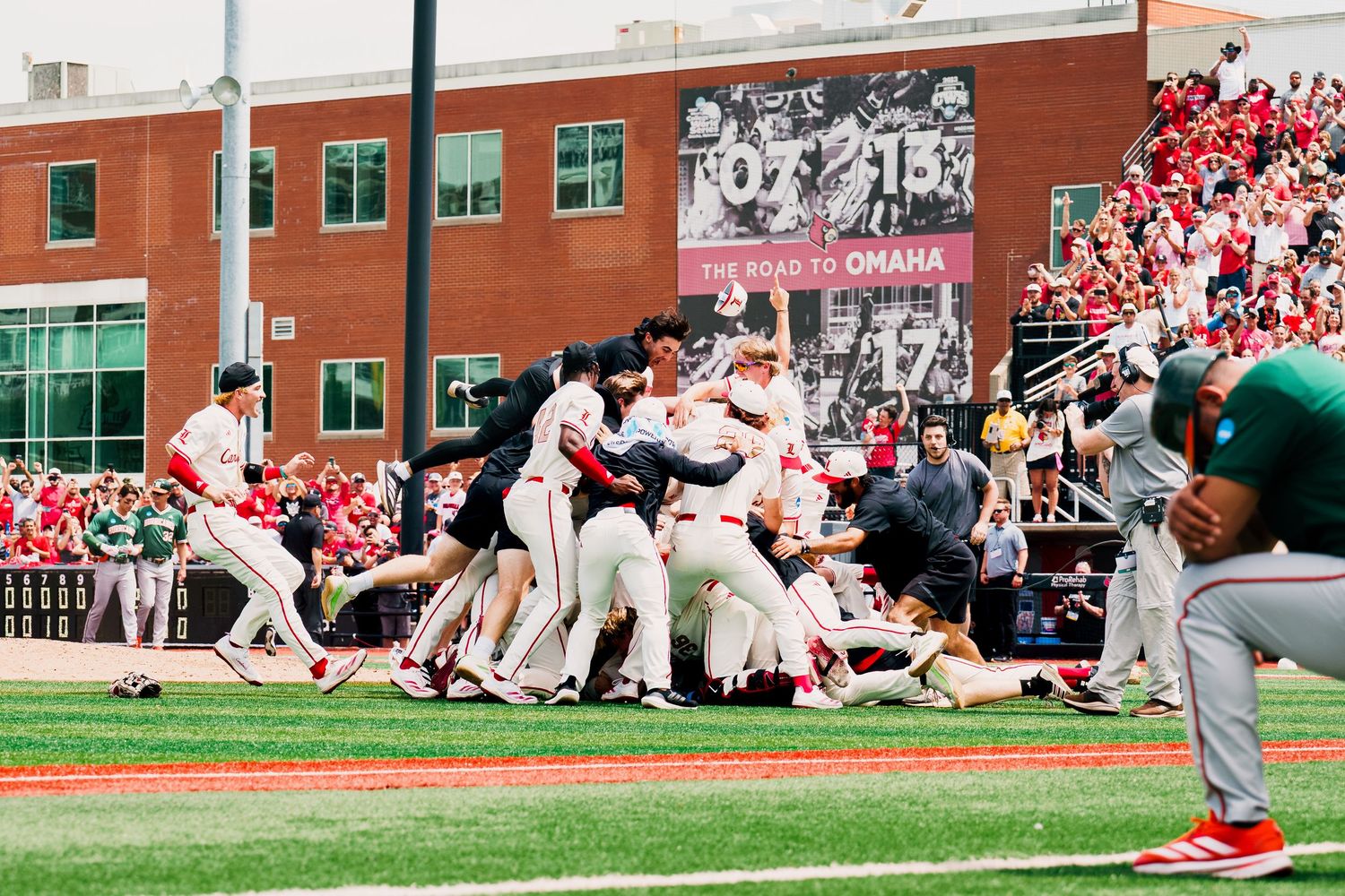 Baseball players celebrate on the field after a game-winning play at a stadium with red seats in the background.