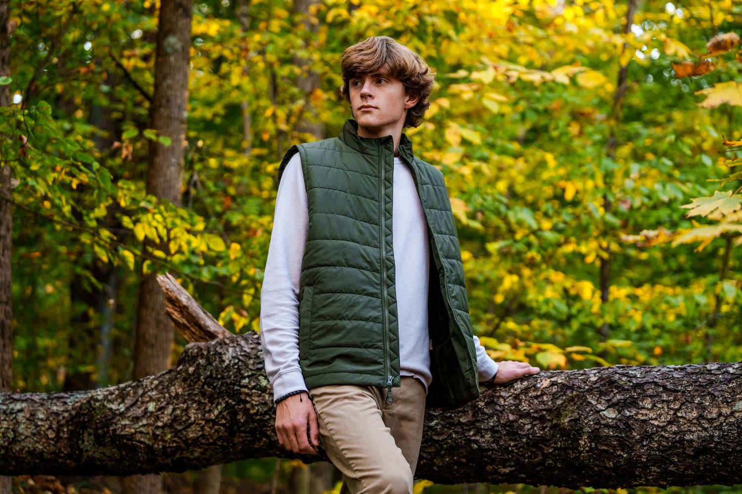 Person in a green vest poses in front of autumn foliage during outdoor photo session.
