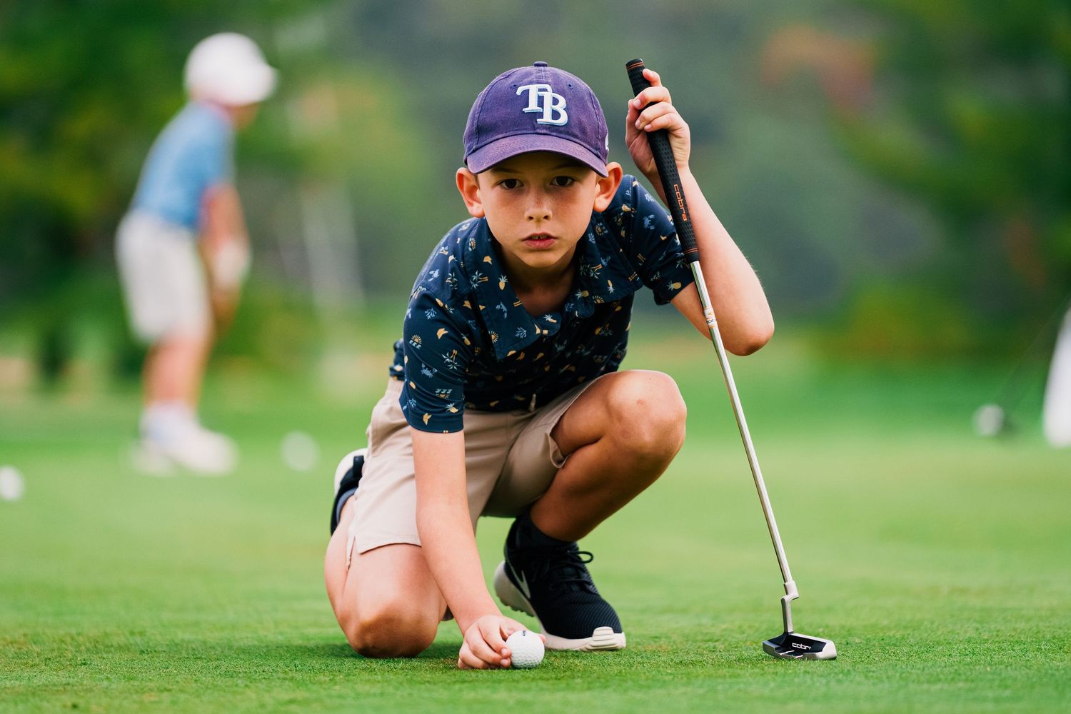 Golfer crouches low to analyze the putting line on a lush green golf course.
