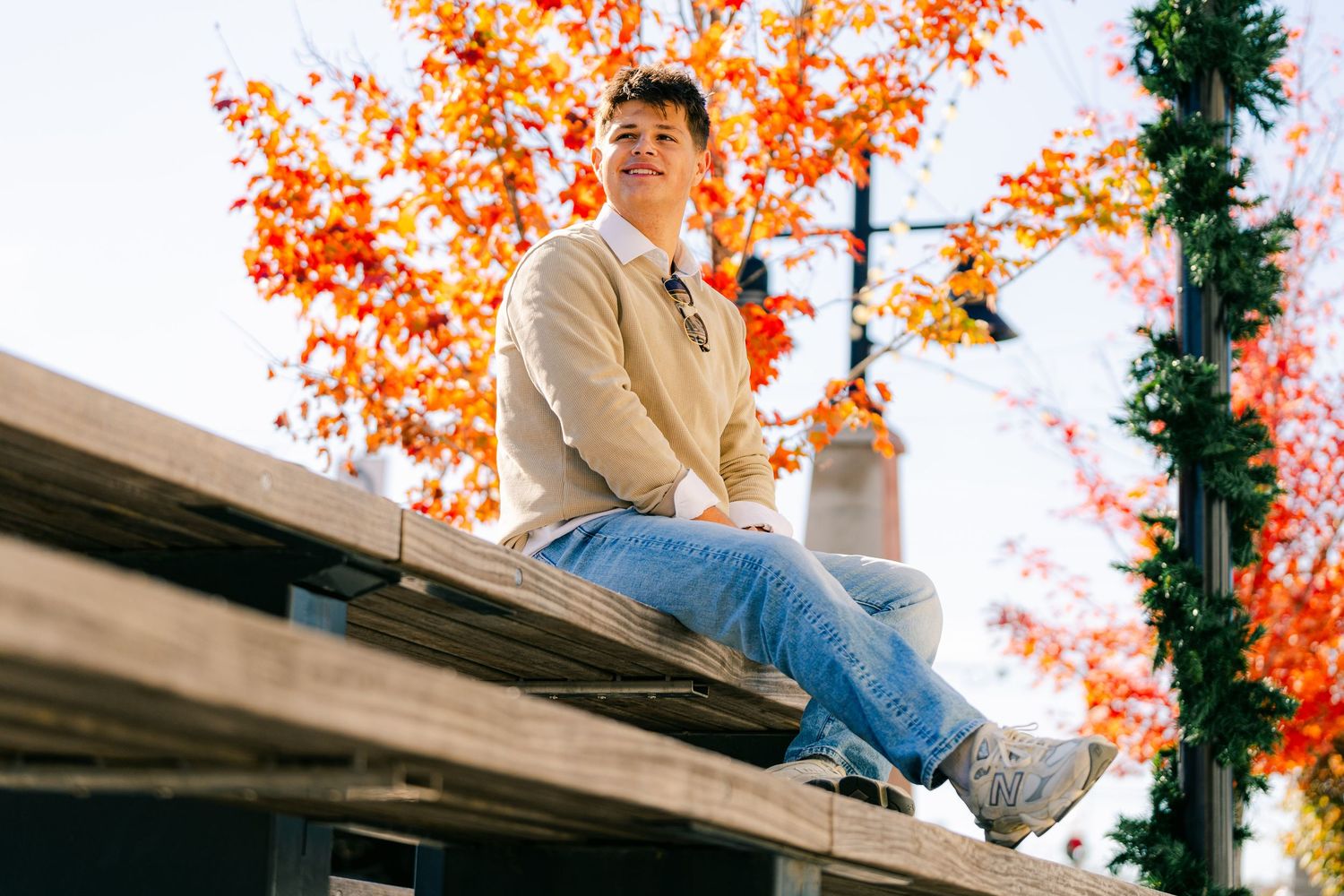 Person sitting casually on a rooftop during autumn with orange foliage in background.