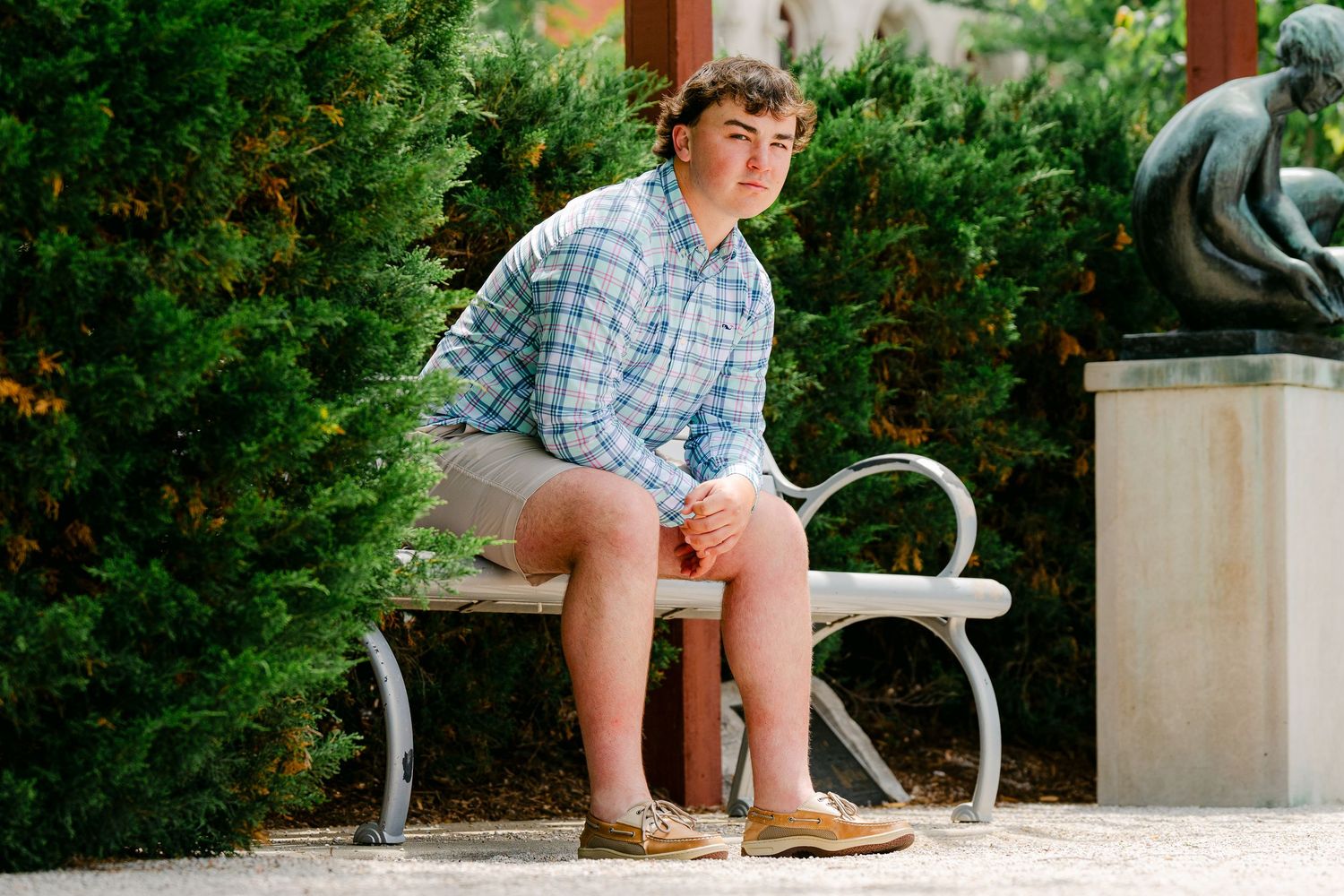 Person sitting on concrete bench in casual summer attire against green landscaping.