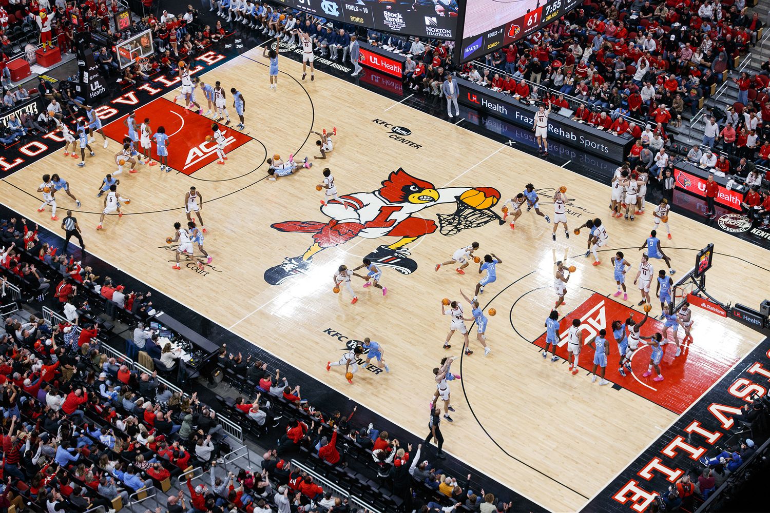 Aerial view of a professional basketball game in progress on a wooden court surrounded by red and black stadium seating.