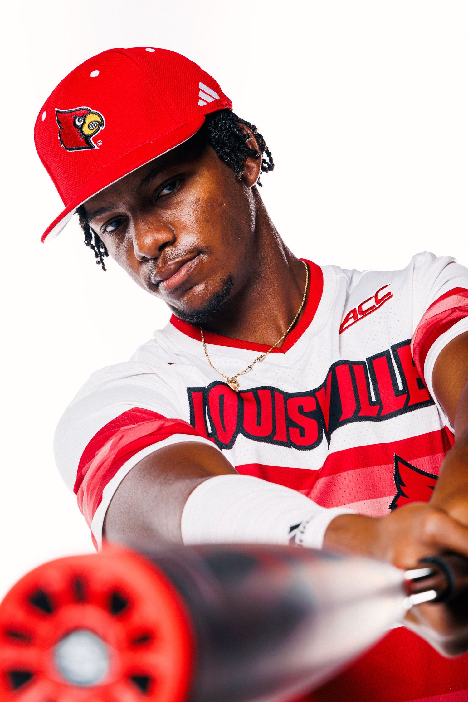 Louisville Cardinals baseball player in red team cap and white uniform with red accents poses for athletic portrait.