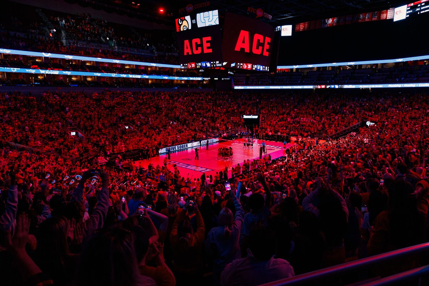 A panoramic view of a packed indoor arena illuminated in red lighting during a live event.