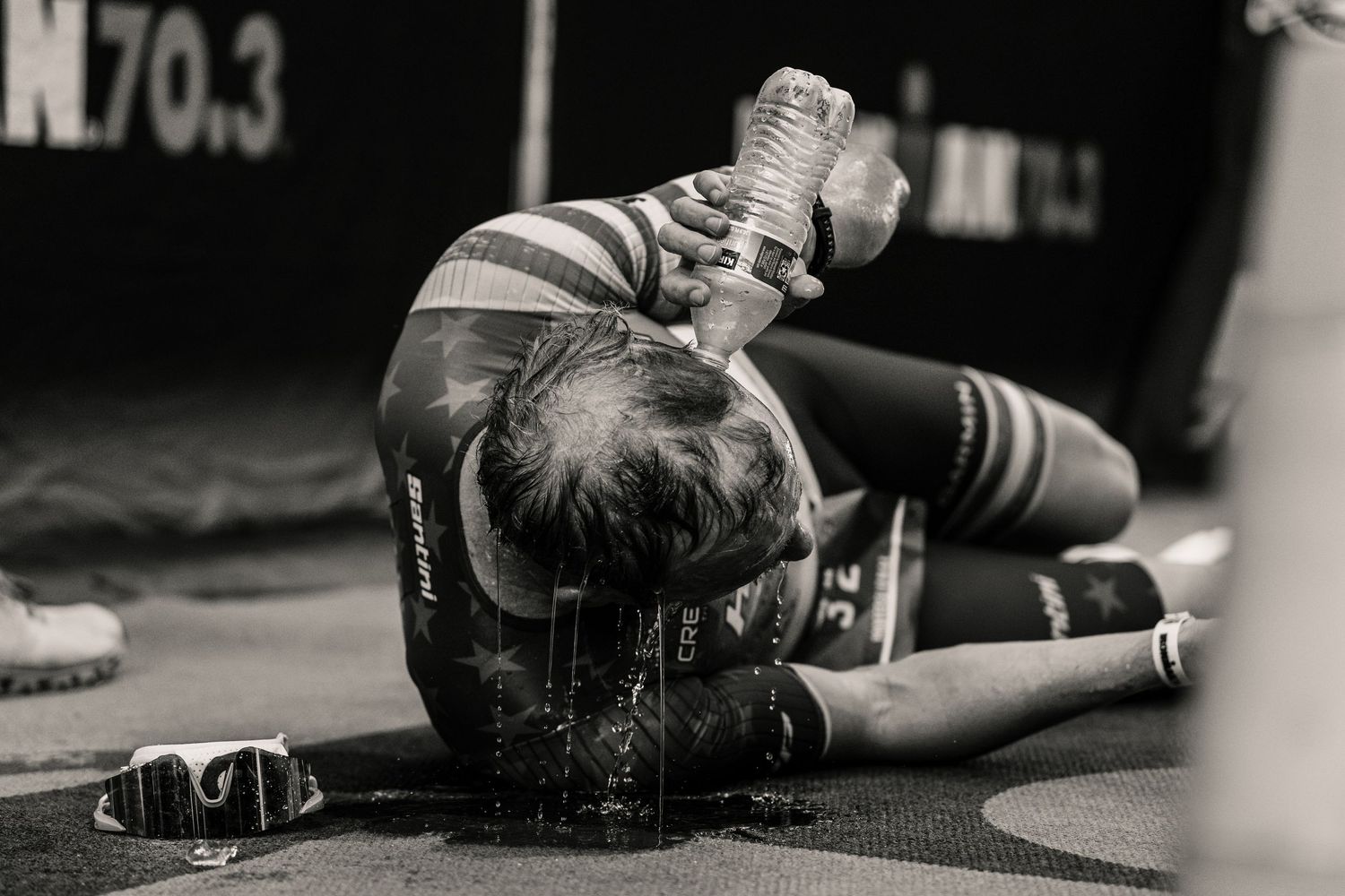 A black and white photo shows an athlete lying on a mat pouring water over their head during a workout.
