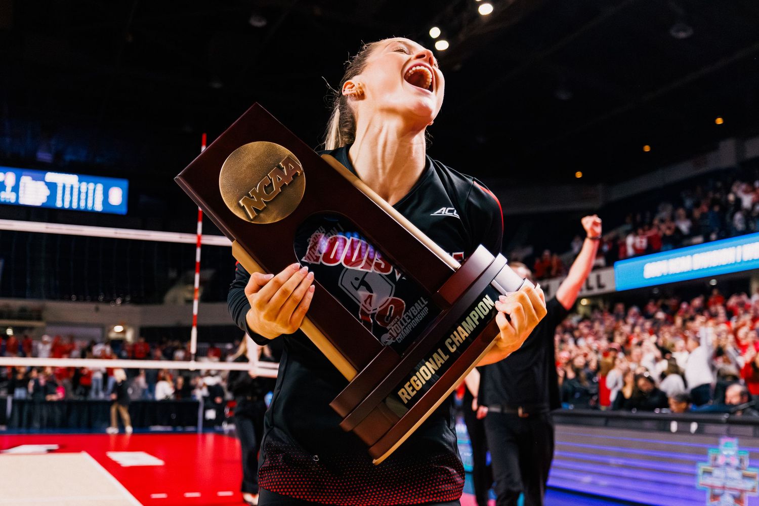 A person celebrates with the NCAA championship trophy on a basketball court after winning the national title.