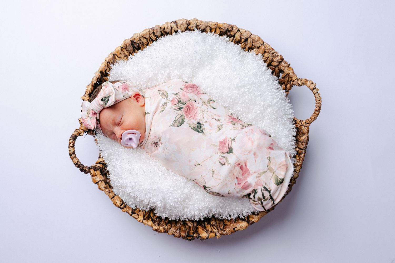 Newborn baby sleeping peacefully in woven basket with white bedding.