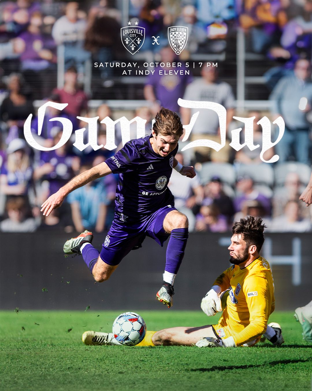 Soccer player leaps over sliding goalkeeper during competitive match at Lynn Family Stadium.