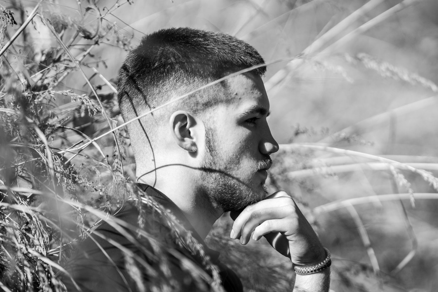 Artistic black and white portrait photograph showing a contemplative profile among tall grass.