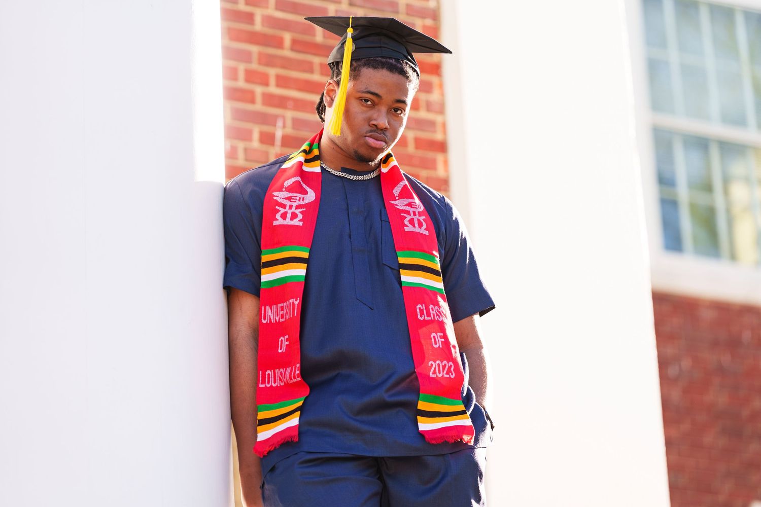 On a brick background, person wears a navy shirt and red lanyard in lifestyle portrait.