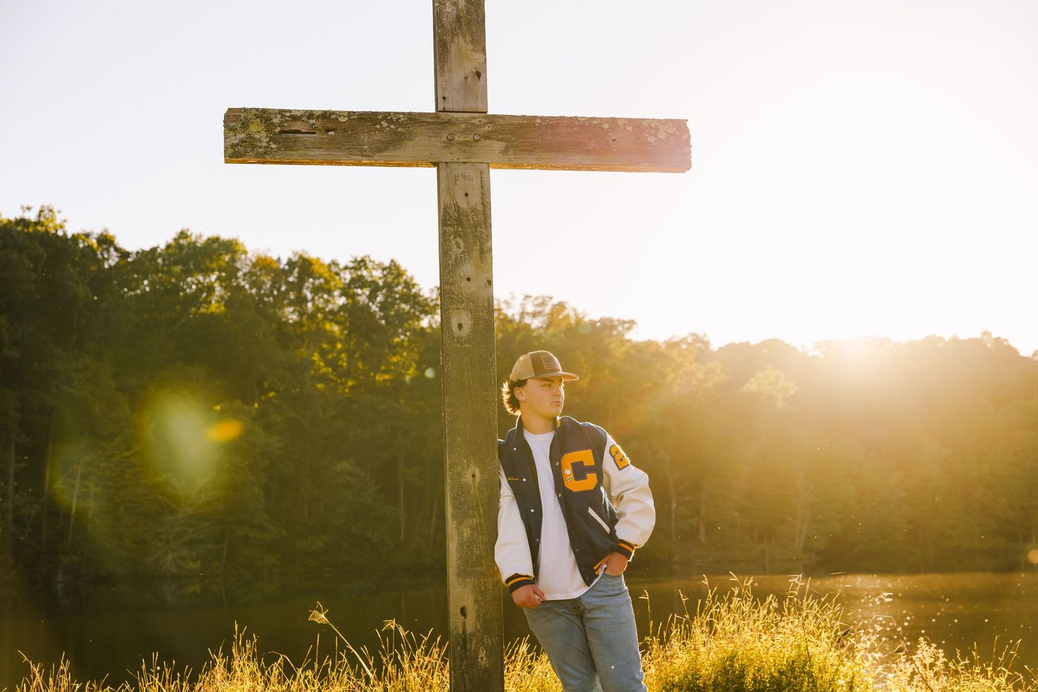 Silhouetted figures walk near wooden cross at sunset in grassy field.