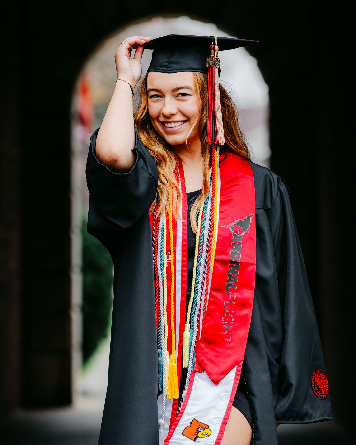Graduate in cap and gown with red stole and honor cords celebrating at commencement ceremony.