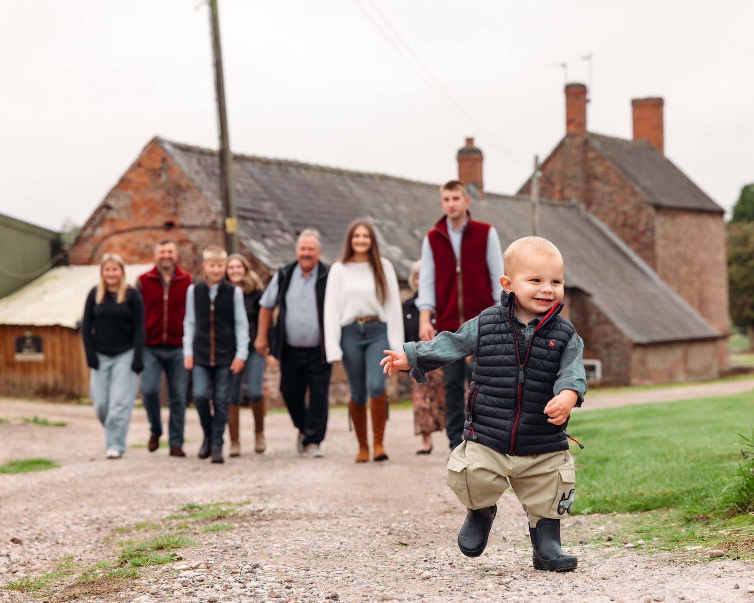 Young child walking independently on country path with others in background.