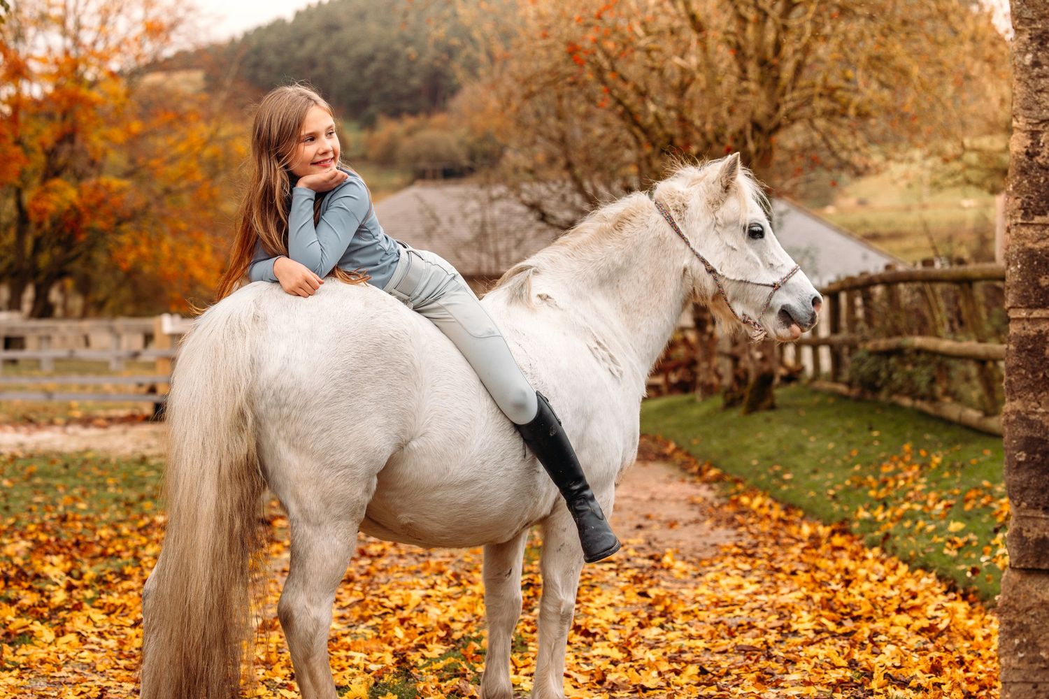 White horse and rider walking through autumn leaves in a scenic fall setting.