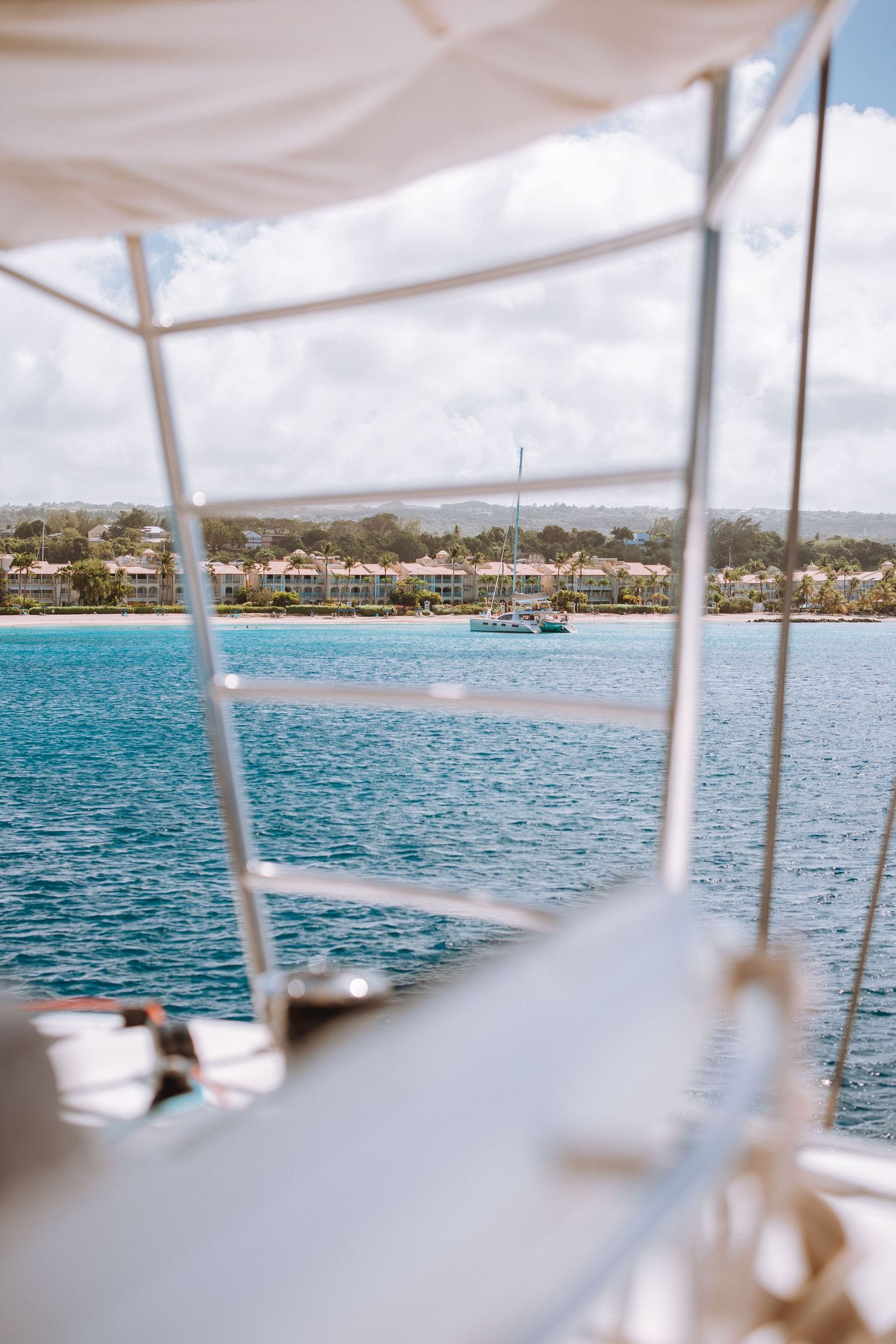 View of tropical blue waters and coastline from boat deck with white canopy.