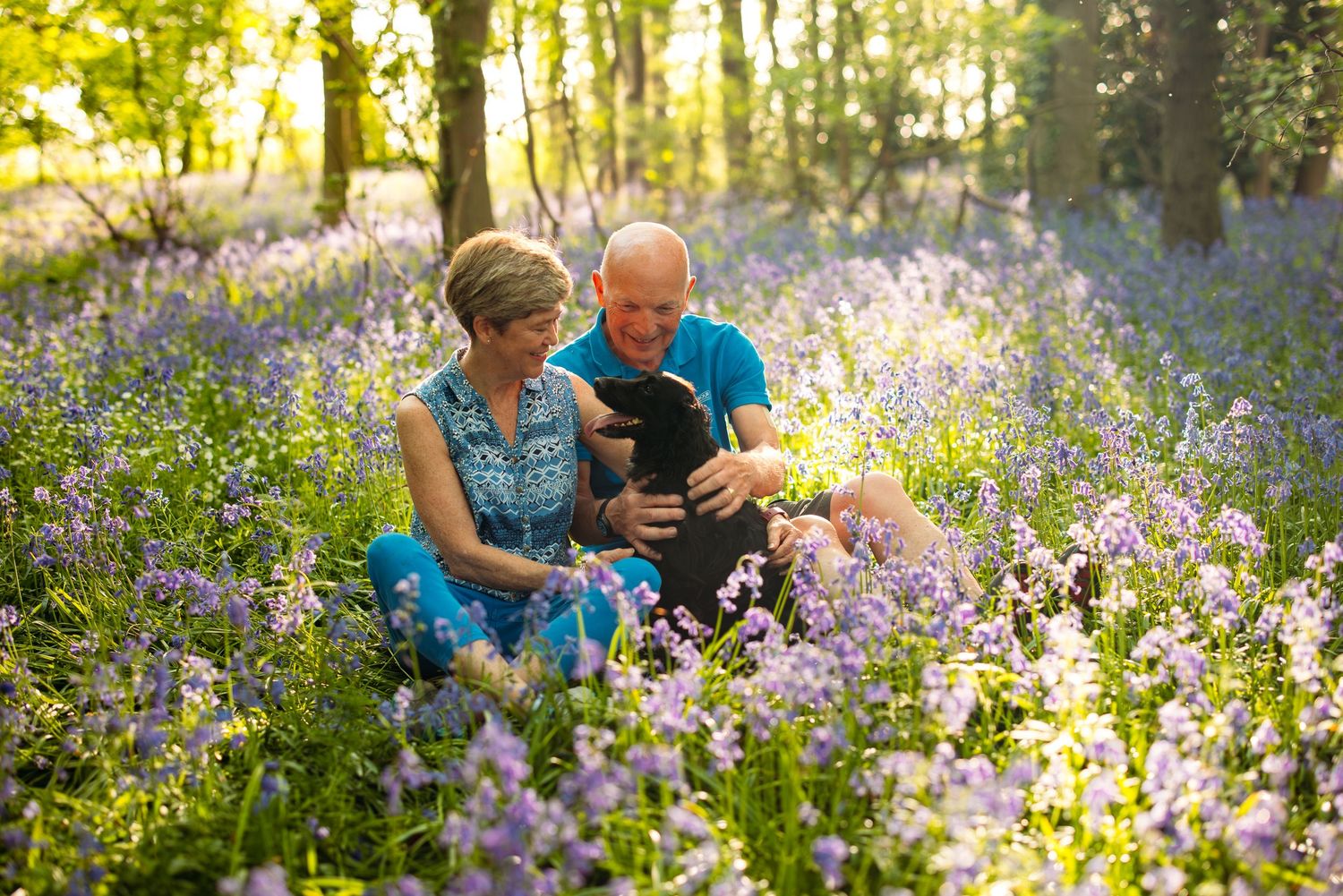 A couple sits among blooming purple wildflowers in a spring woodland setting.