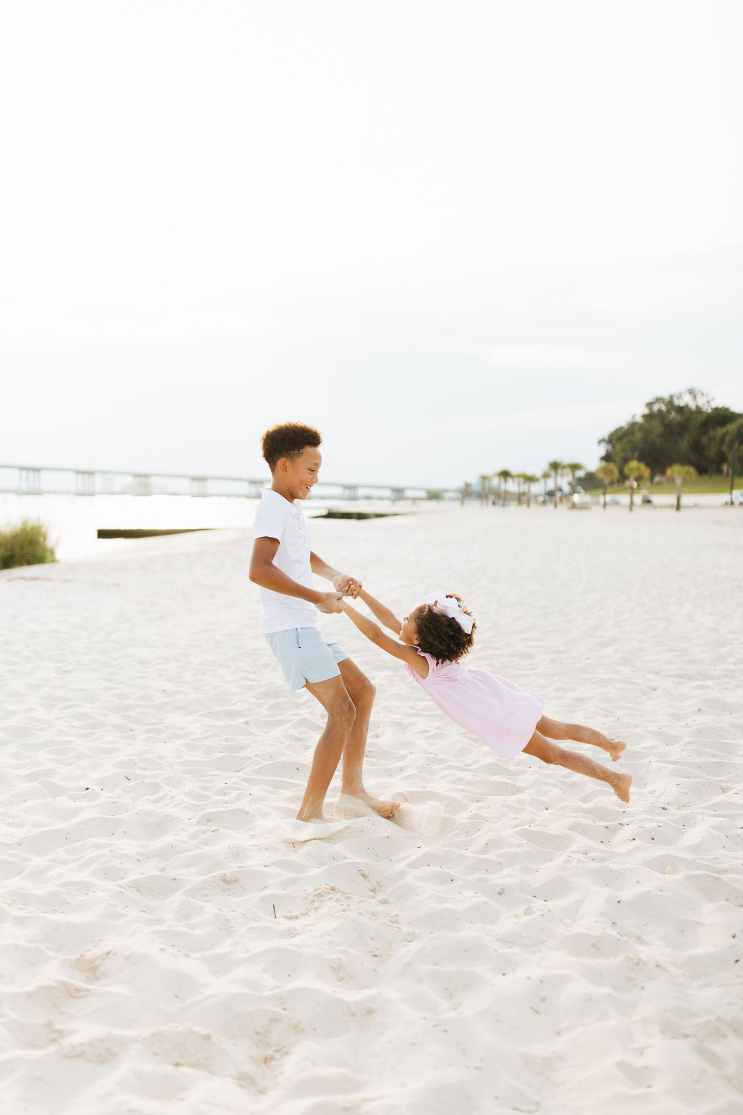 Playful sequence of beach photos showing family members lifting and spinning on white sand.