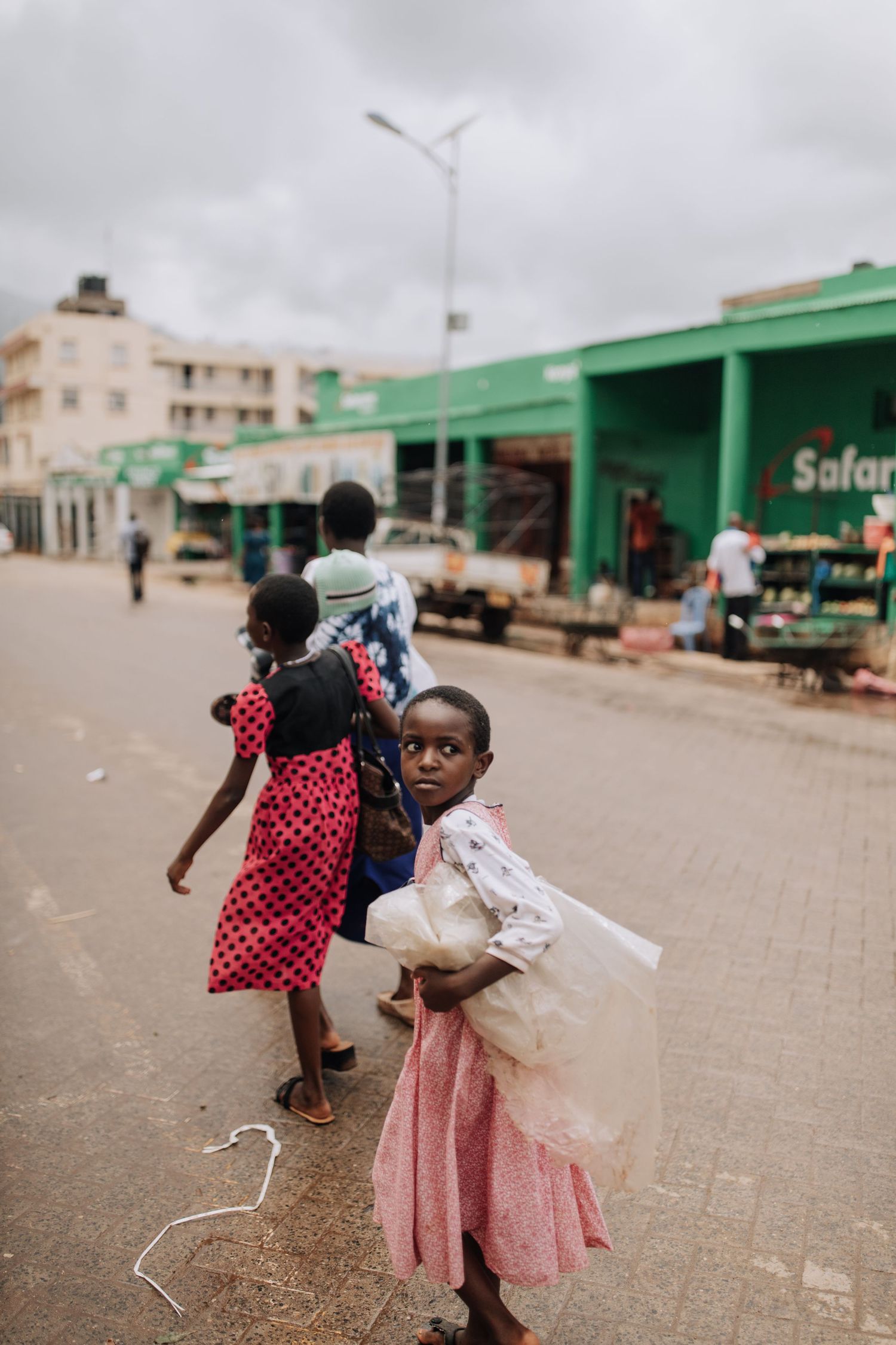 Children in pink dresses play and twirl while running outside a building with green painted walls in Africa.