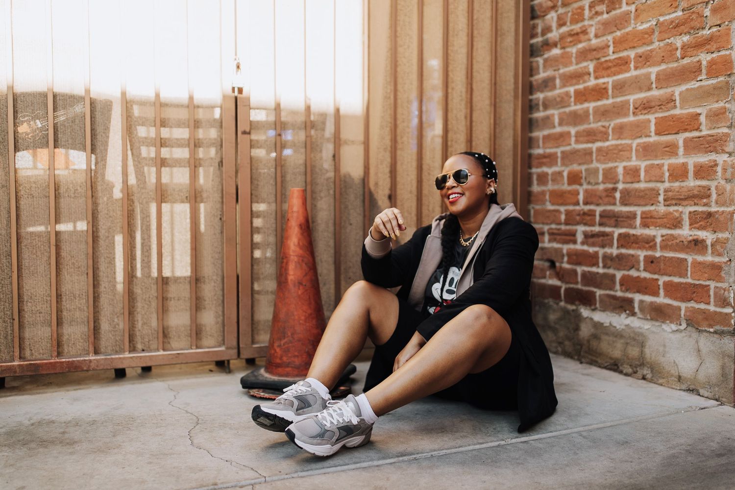 Two people lounging against a red brick wall, wearing athletic clothing and sunglasses.