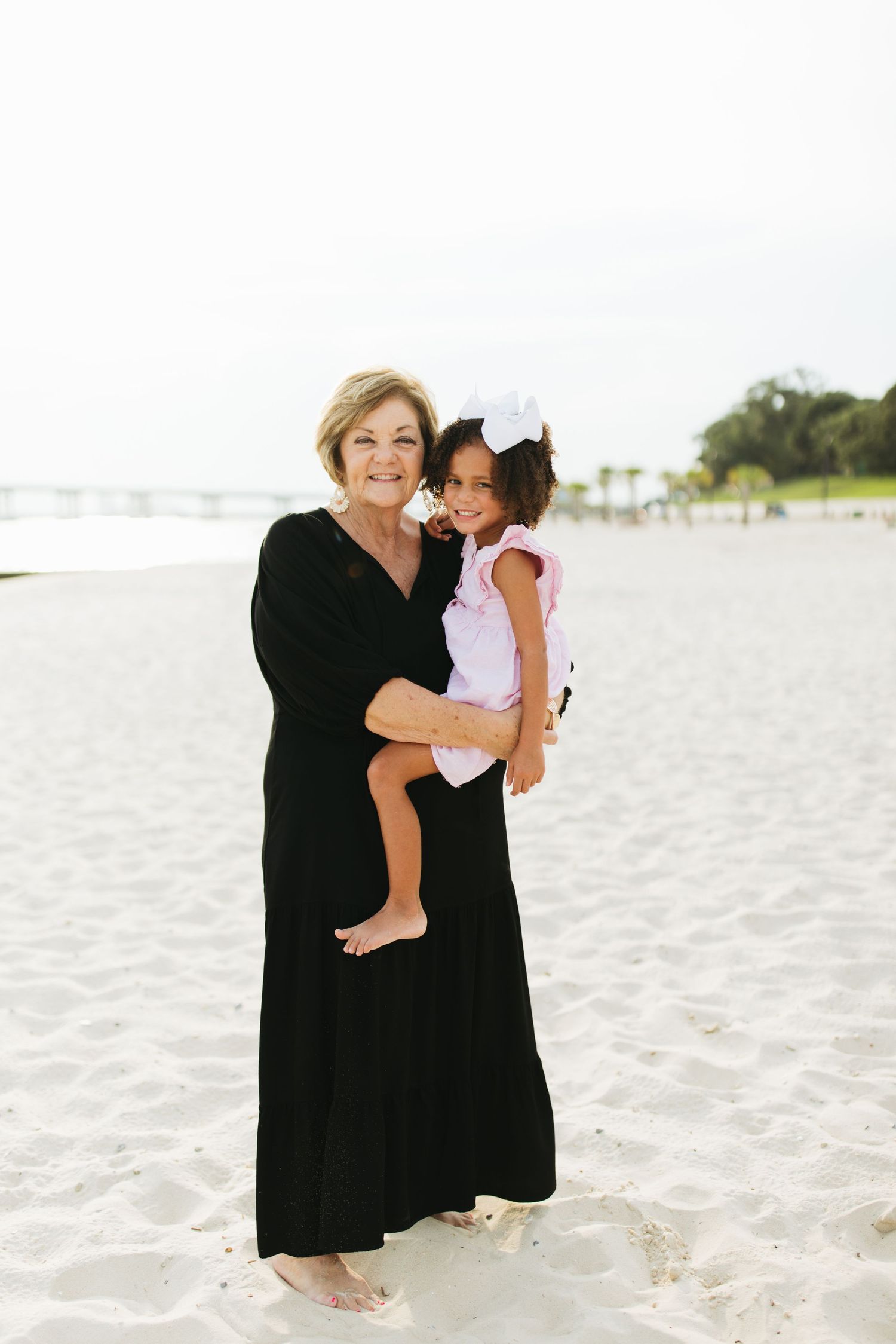 A heartwarming beach portrait showing a warm embrace on white sand with palm trees in the background.