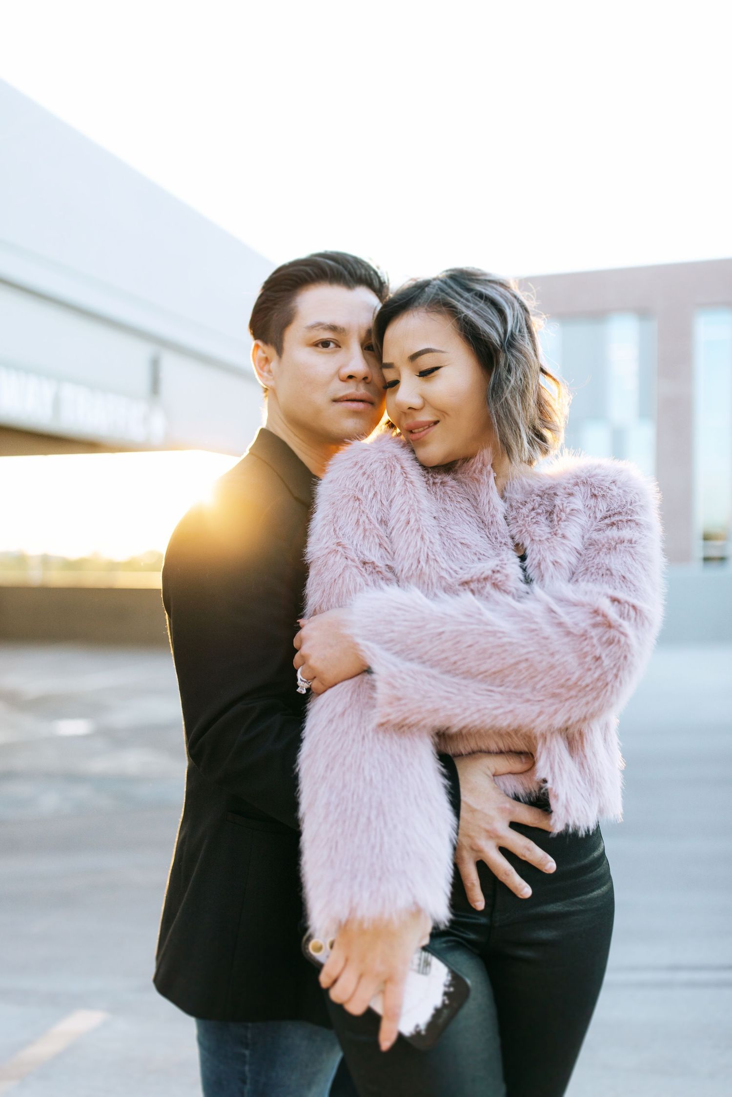 A romantic couple embrace wearing contrasting black and pink outfits during an outdoor photo session at sunset.