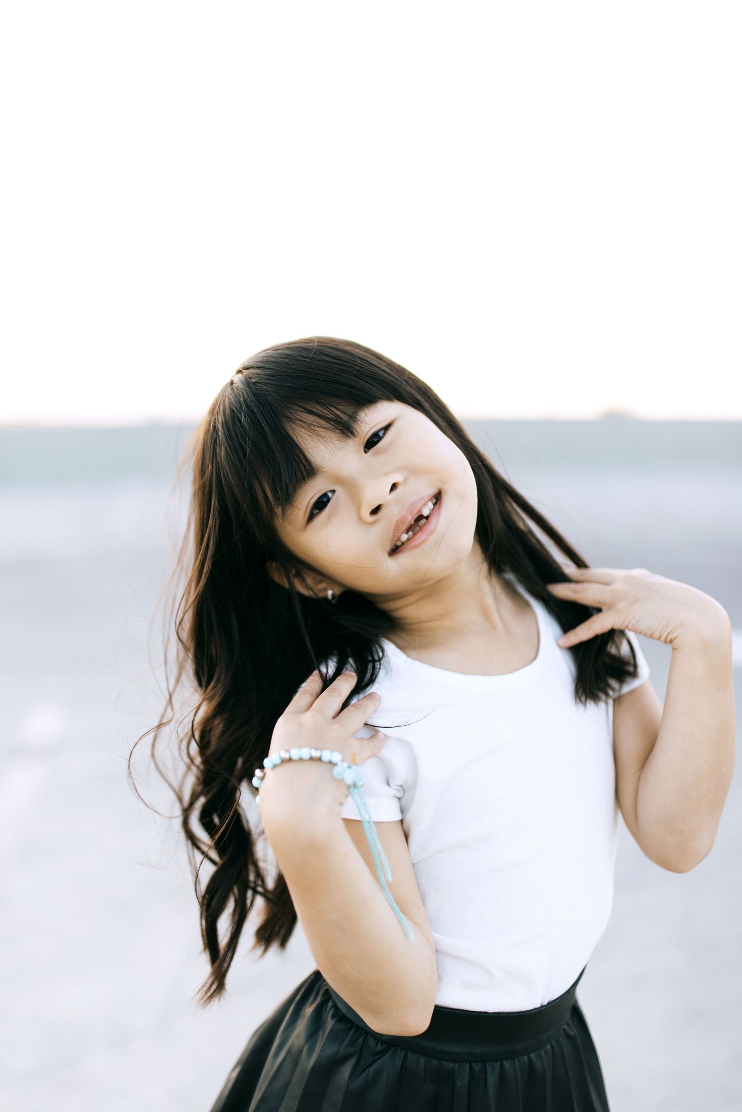 A child poses playfully in a monochromatic photoshoot wearing a white tank top and dark skirt.