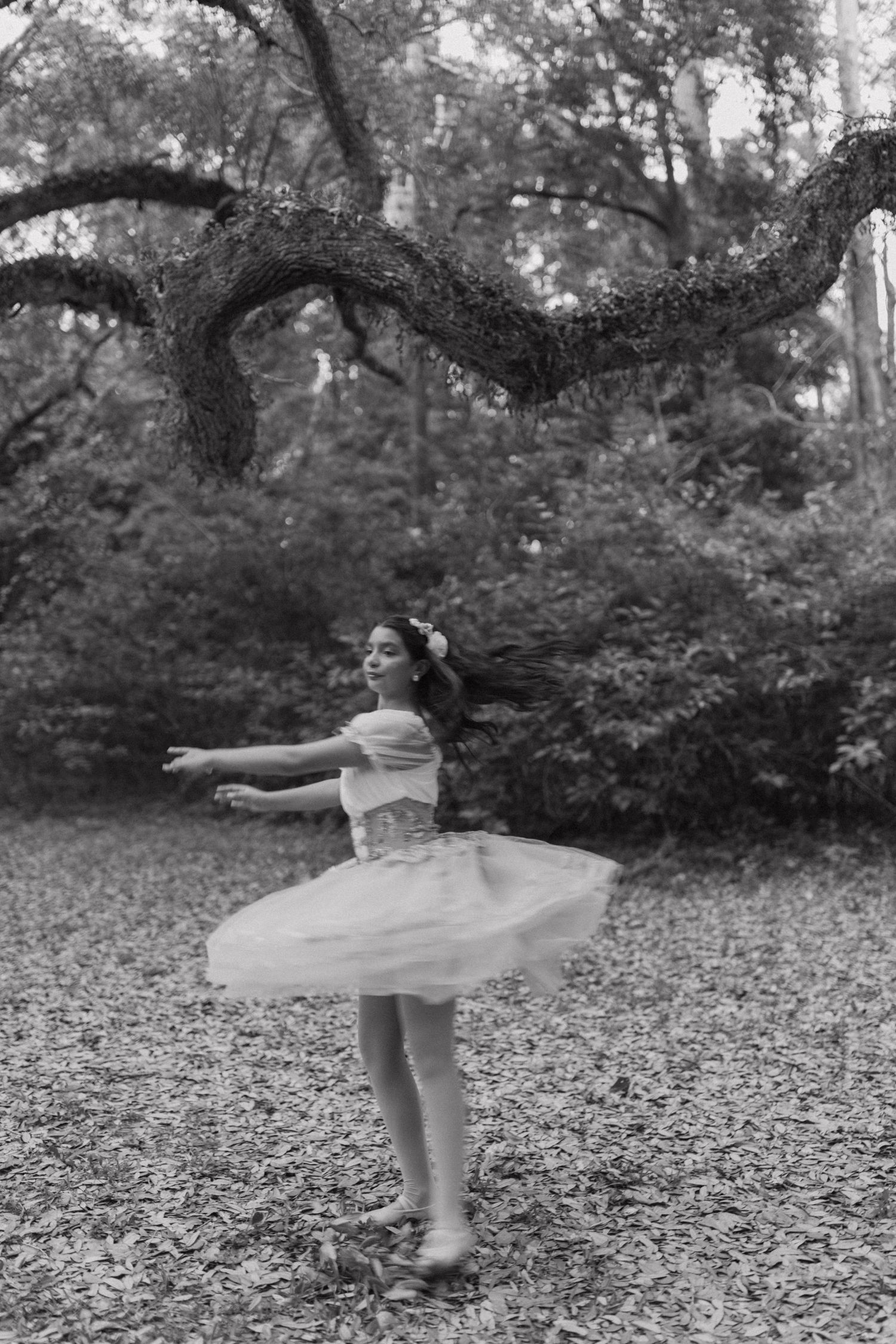 A graceful dance performance captured in black and white showing fluid movement among trees and fallen leaves.