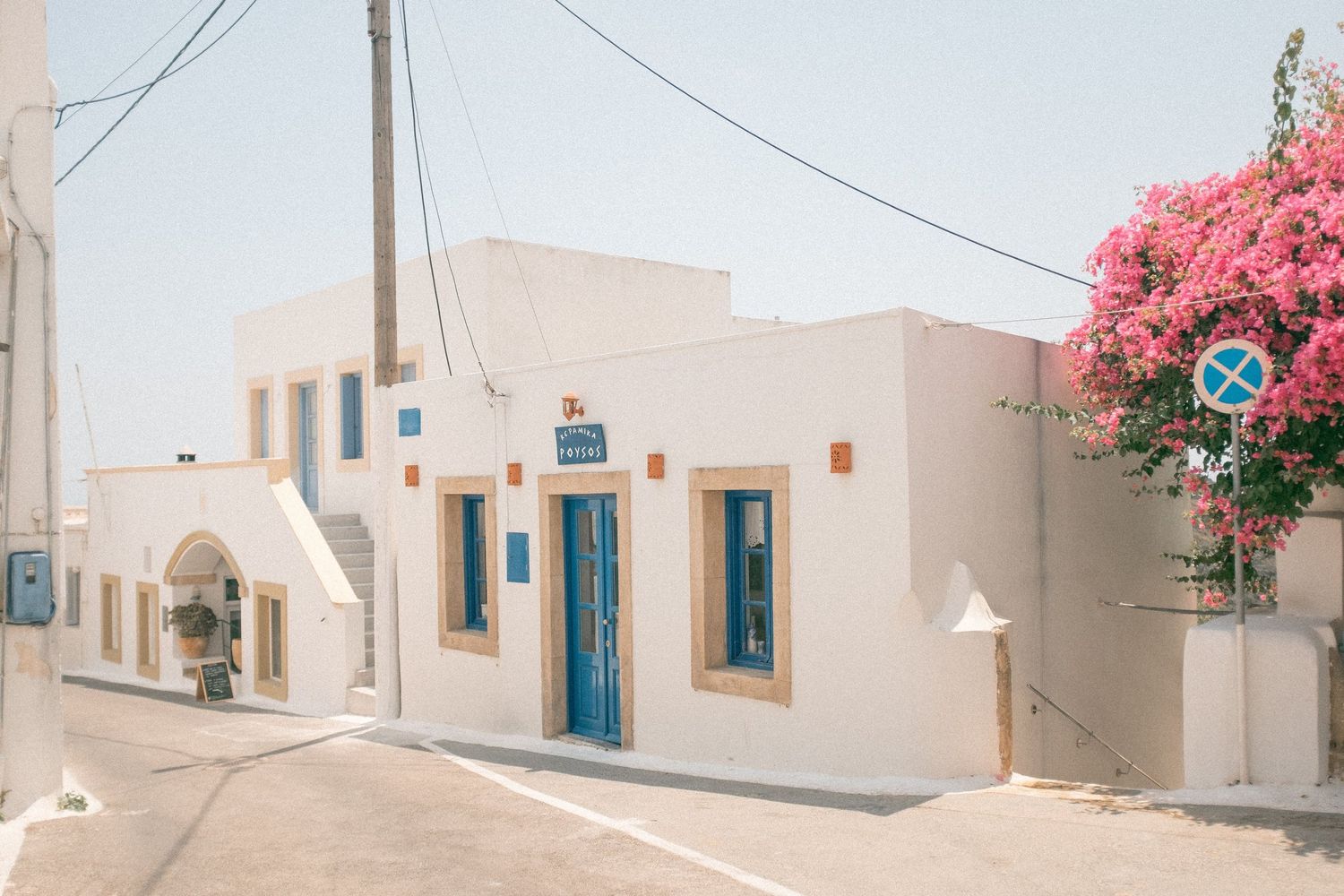 Charming Mediterranean street with whitewashed buildings, turquoise doors, and pink bougainvillea flowers in the corner.