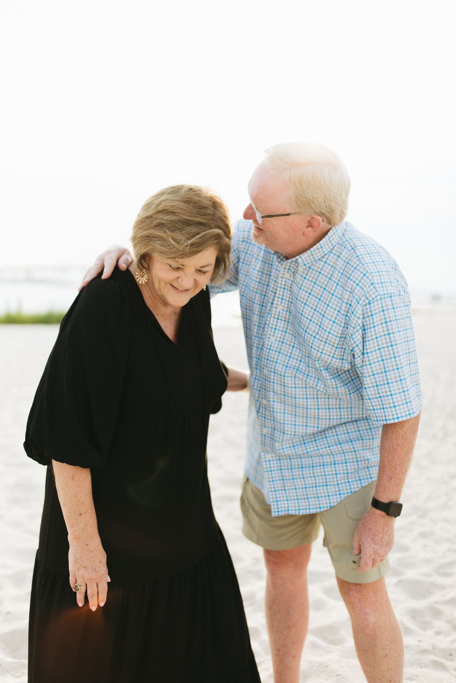 Senior couple shares intimate moment while walking on white sand beach.
