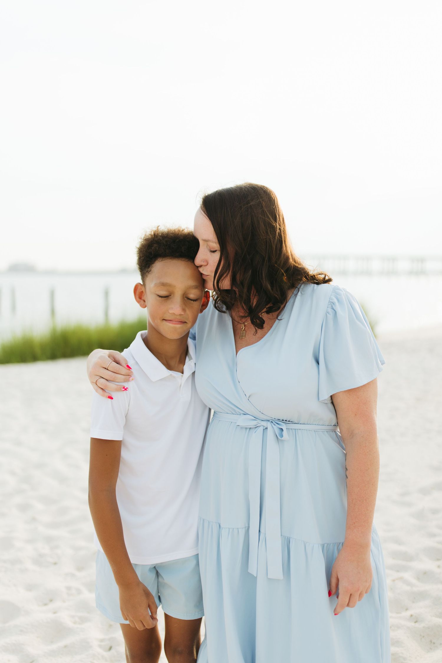 A sweet beach portrait shows tender family moments on white sand with casual blue and white outfits.