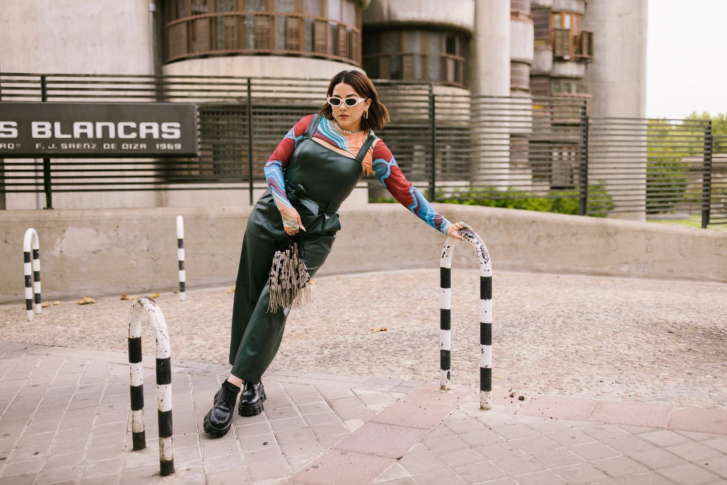 A person performs a series of inline skating tricks and maneuvers on a paved urban path between bollards.